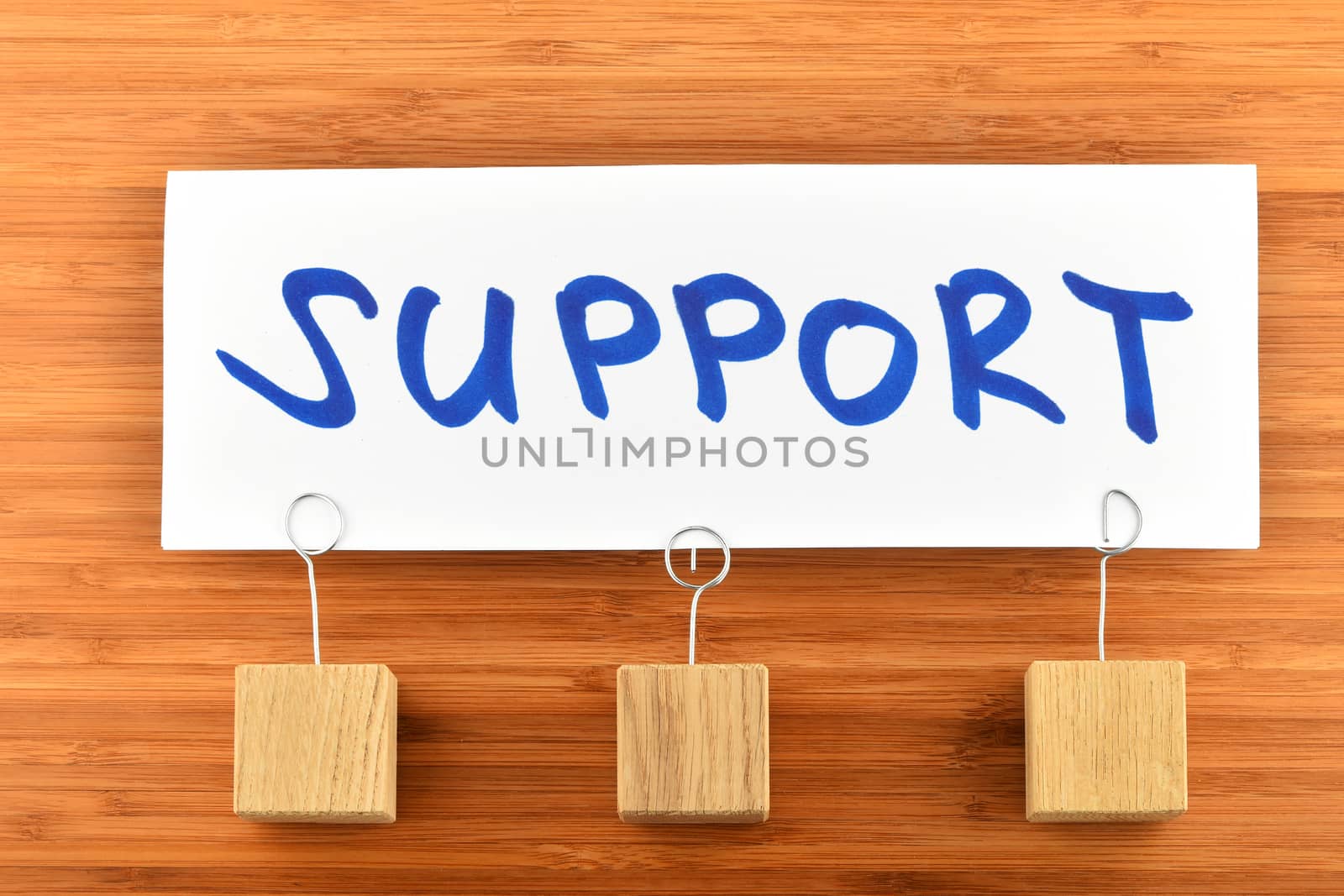 Support, one big white paper note with blue hand written text and three wooden holders on bamboo background for presentation