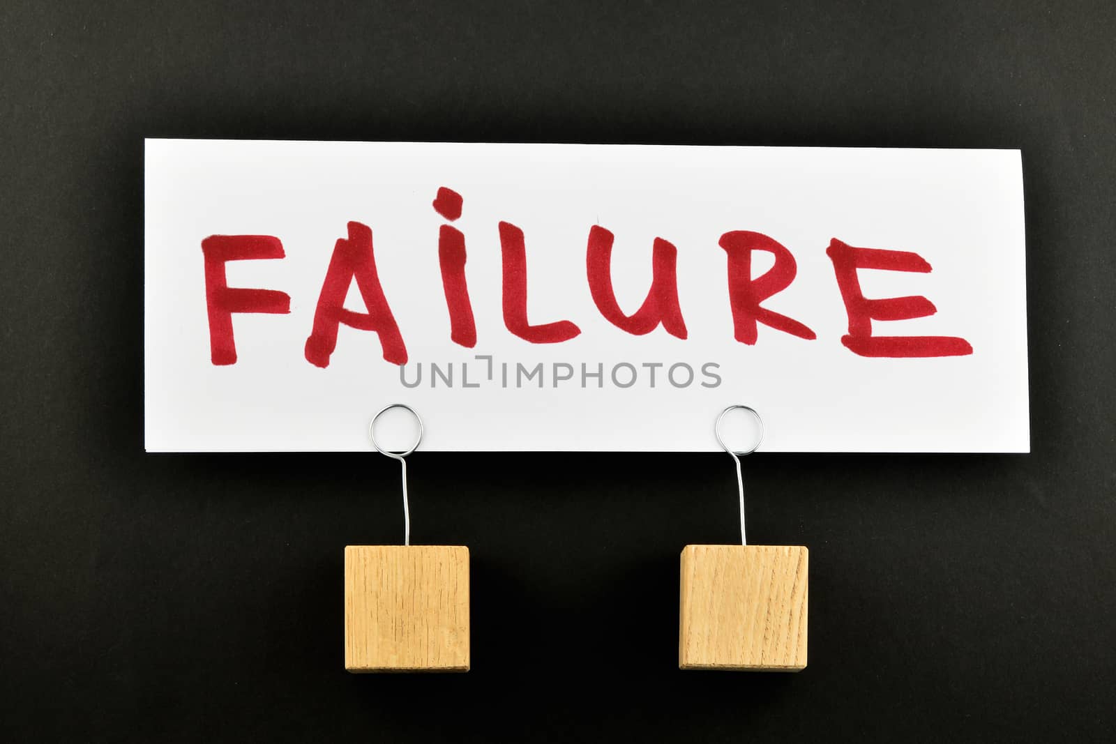 Failure, One big white paper note with two wooden holders and red letters, isolated on black paper background for presentation