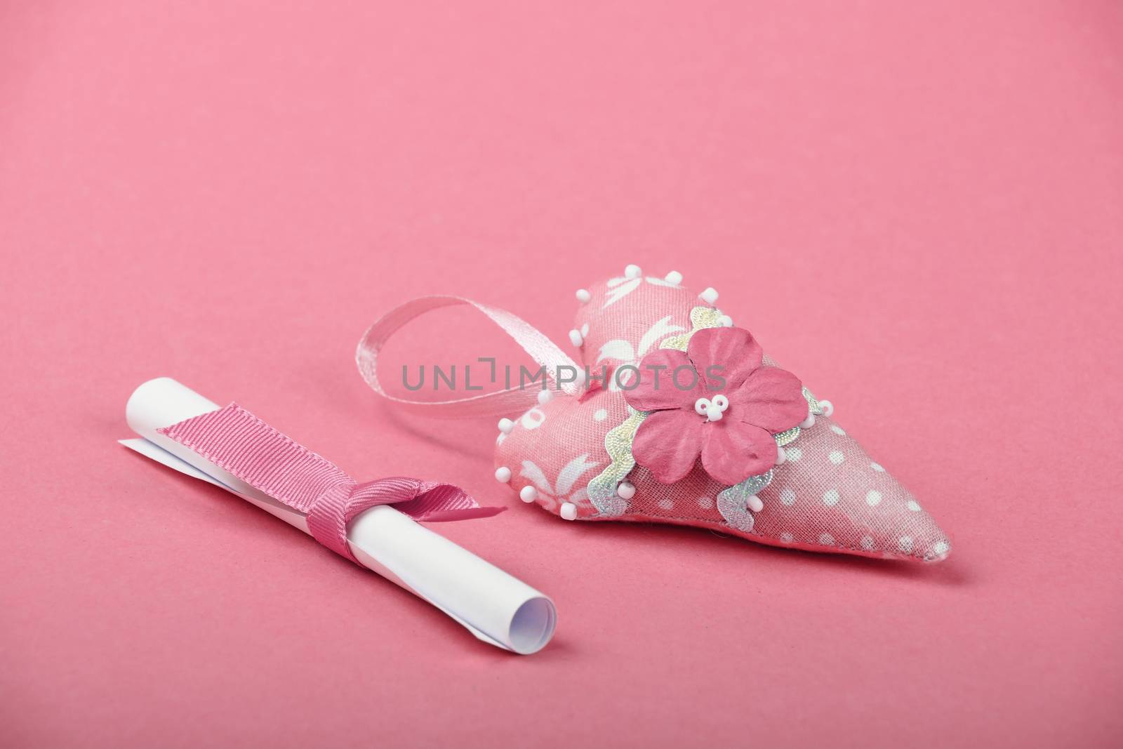 One small white paper scroll love message note with ribbon and heart with flower on rose pink background