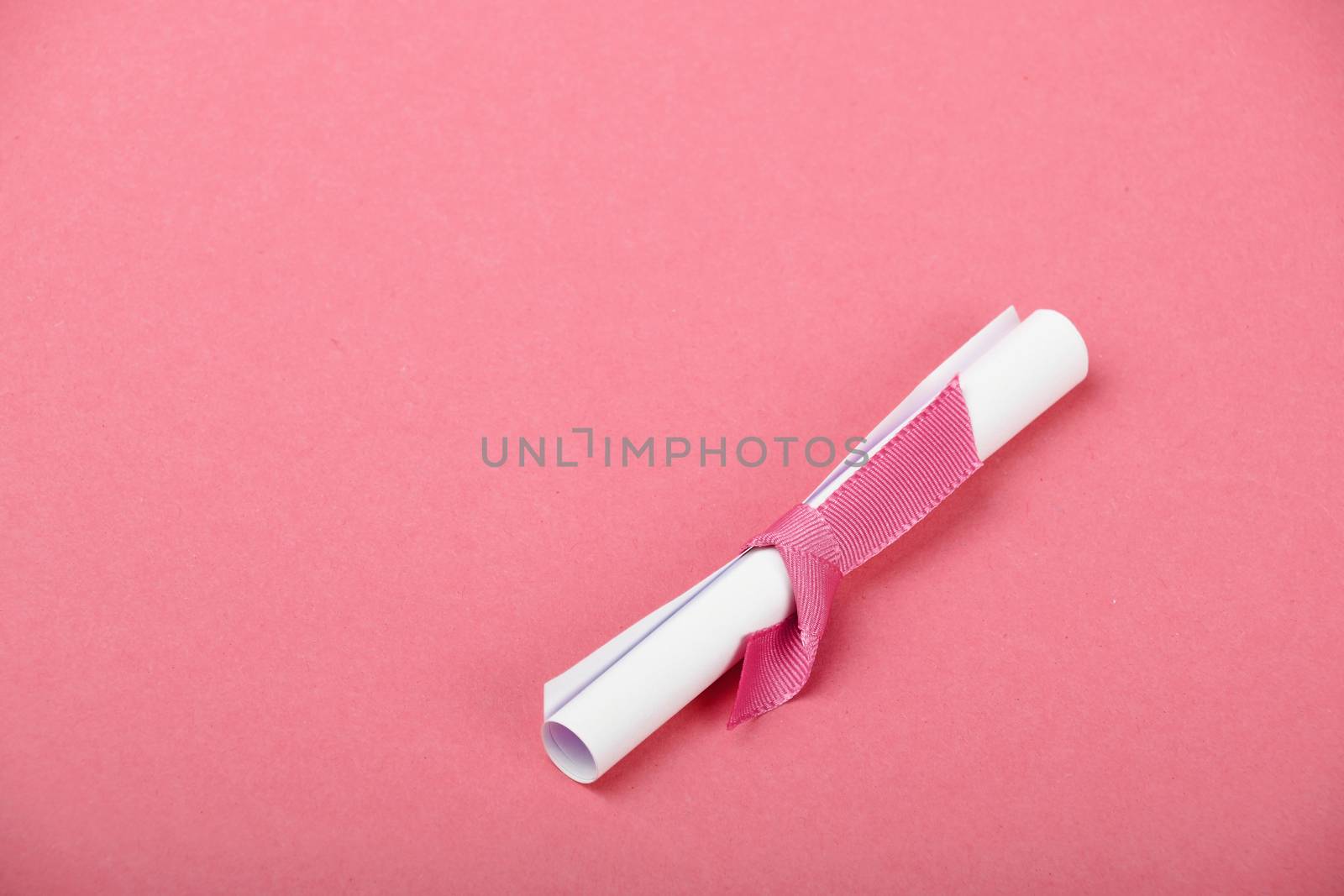 One small white paper scroll love message note with ribbon on tender pink background