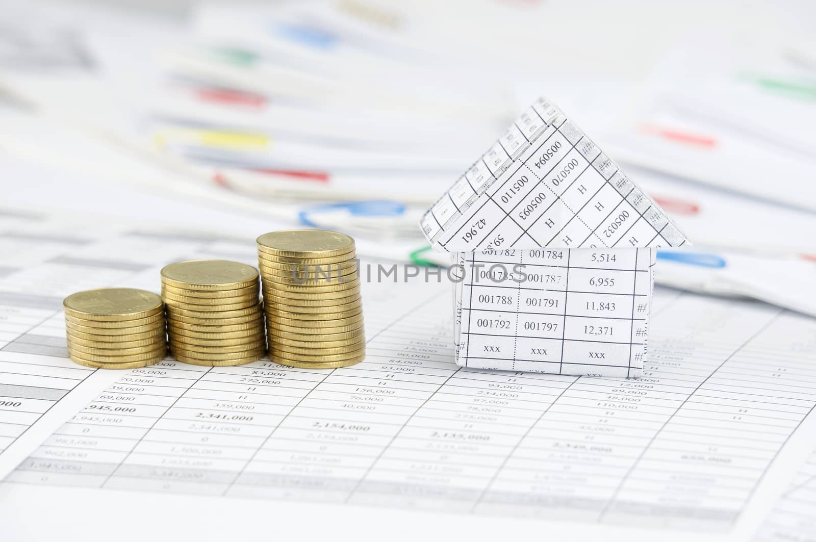 Close up house and step pile of gold coins on finance account have blur step of paperwork with colorful paperclip as background.