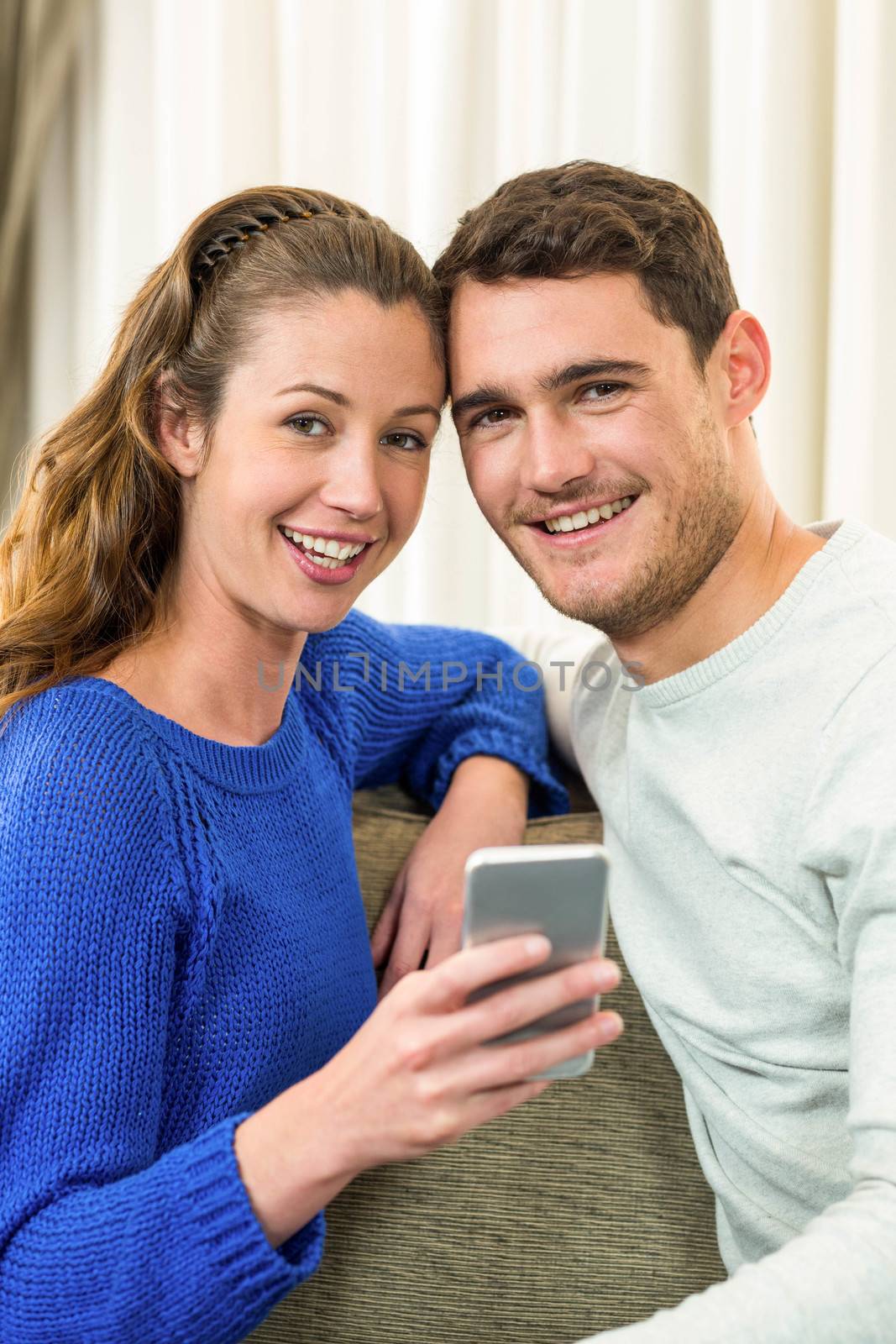 Young couple sitting on sofa and using mobile phone in living room