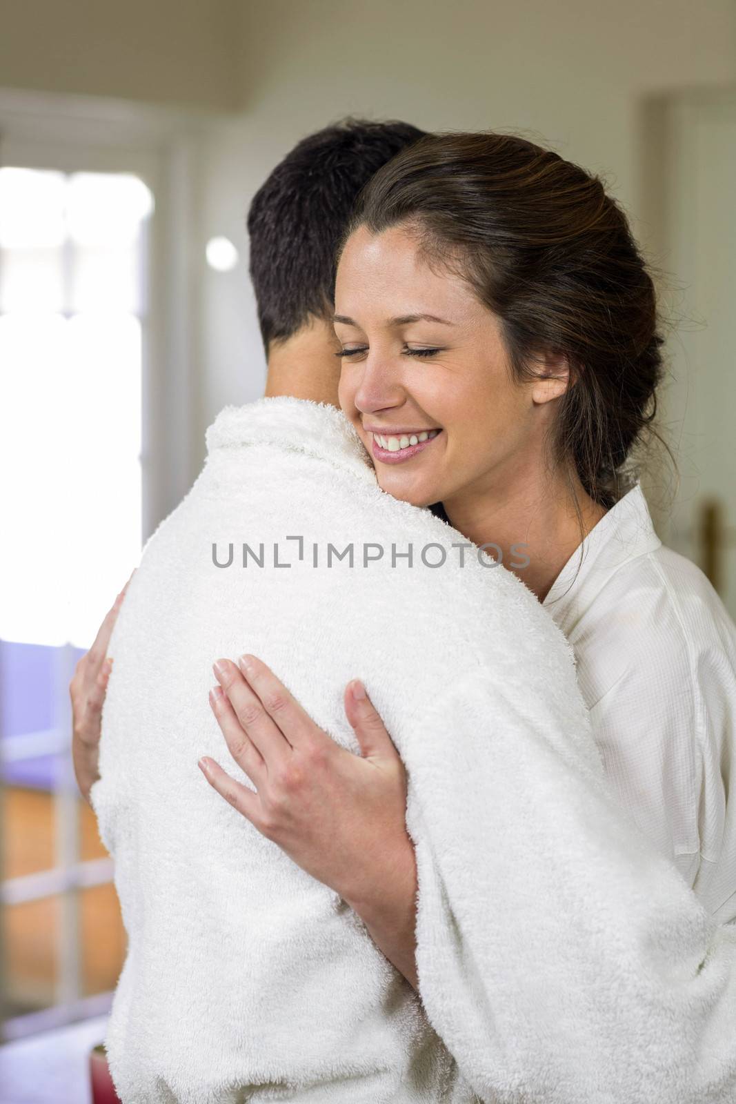 Romantic young couple in bathrobe cuddling each other in kitchen