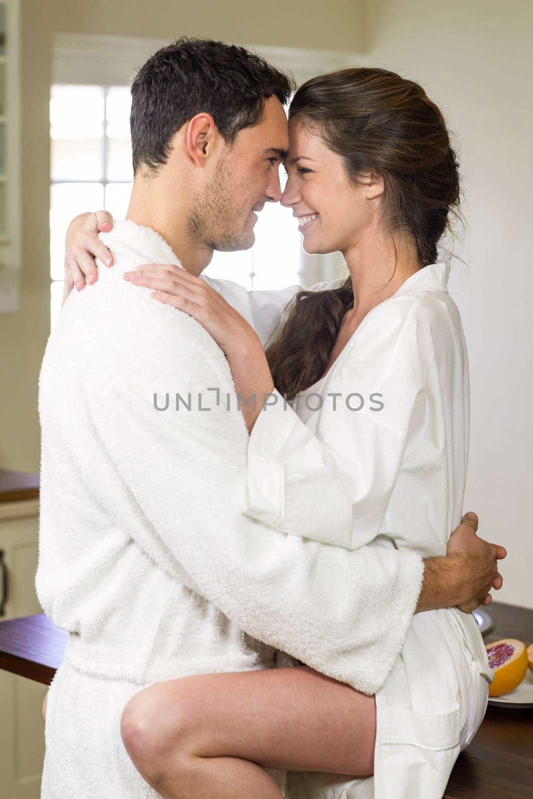 Romantic young couple in bathrobe cuddling each other in kitchen