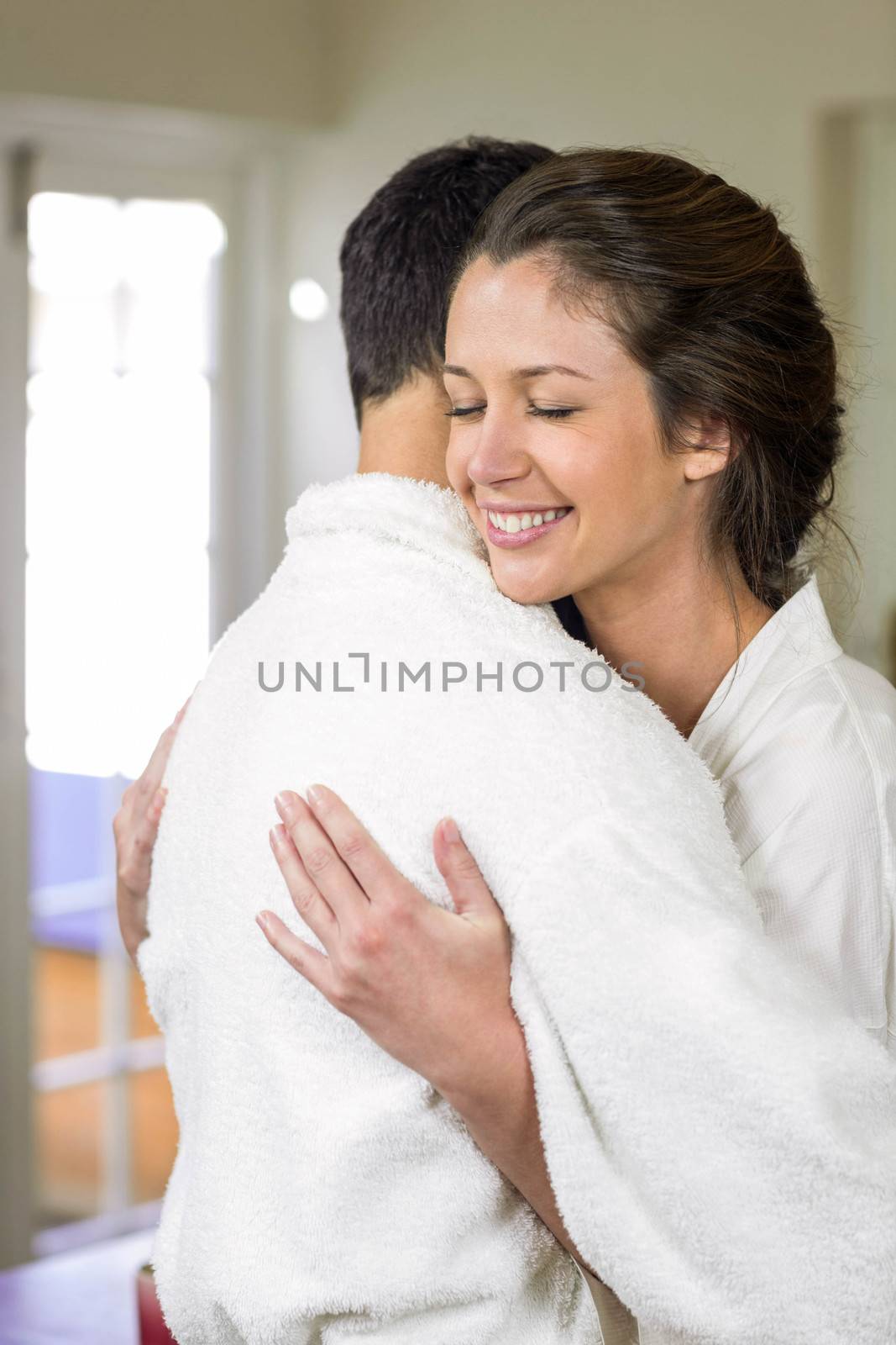 Young couple in bathrobe cuddling each other by Wavebreakmedia