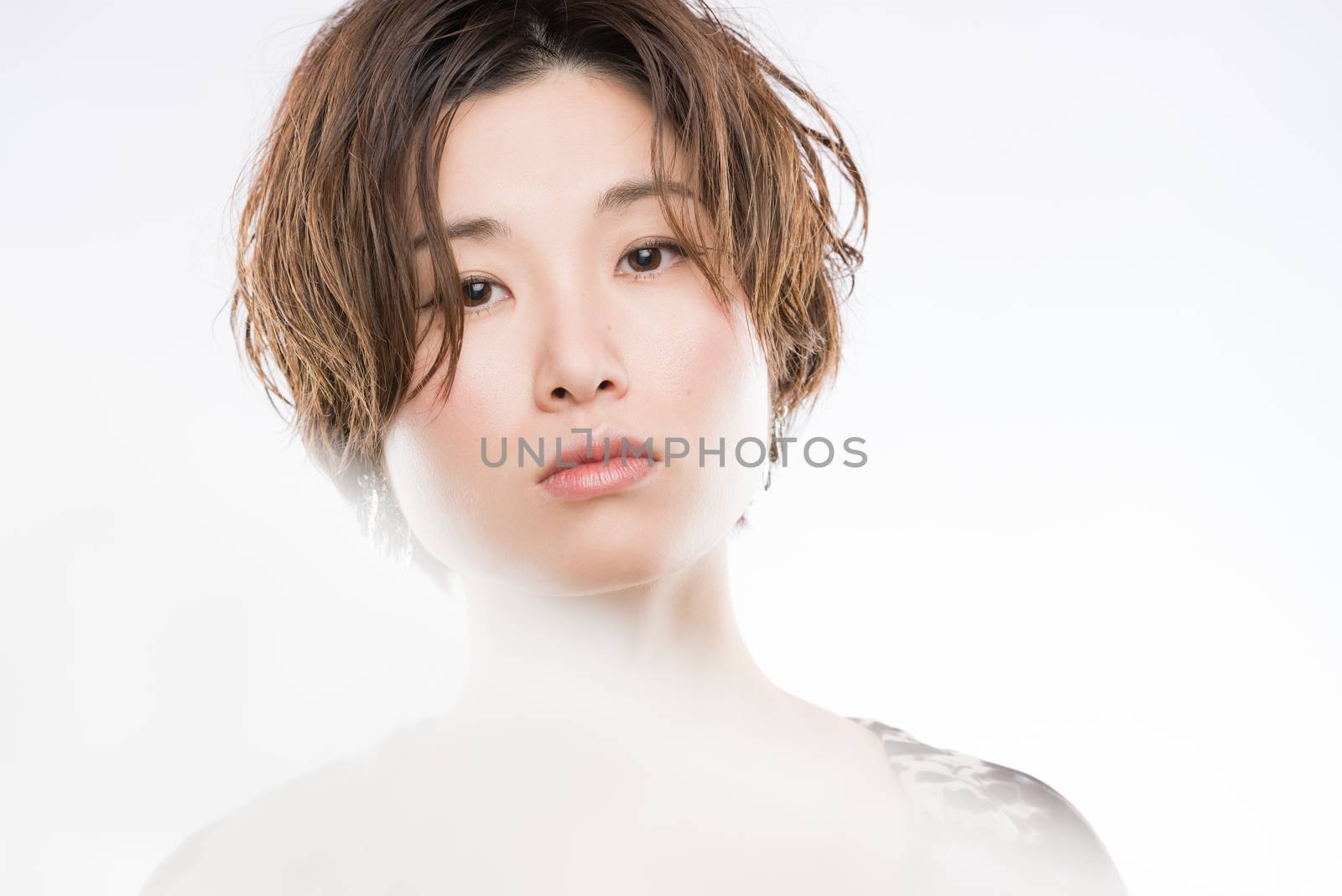 A high key headshot of a young and beautiful Japanese woman with a blurred lace sheet fluttering in front and cutting through the picture for artistic effect shot on a white background.