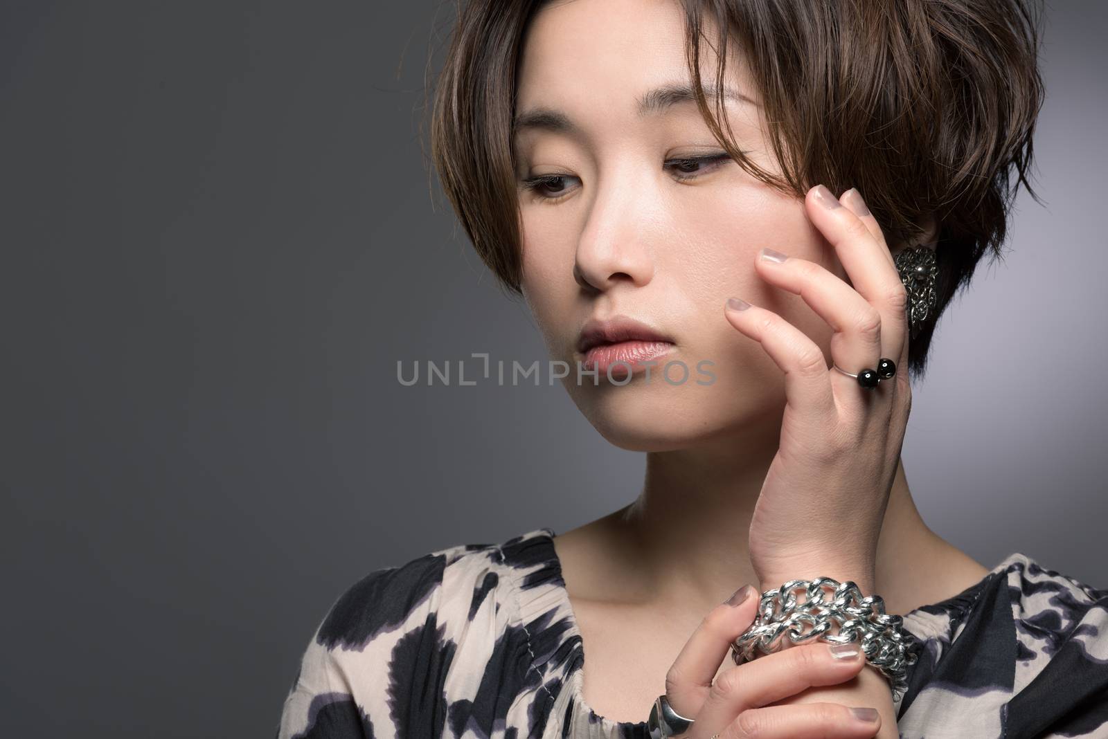 A portrait of a young, beautiful and very fashionable Japanese woman posed gently on a dark background.
