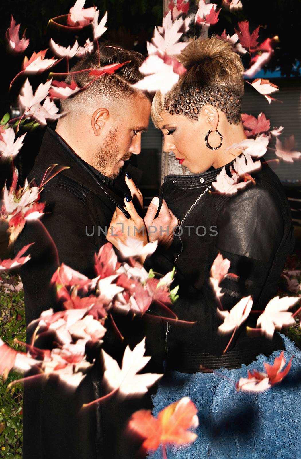 Romantic fashionable young couple caught with blowing leaves. Urban fashion photography. Vertical image.
