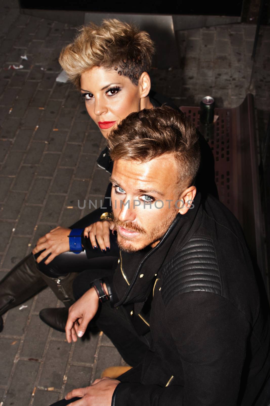 Fashionable young couple sitting at the bus stop with defiant look. Urban fashion photography. Vertical image.