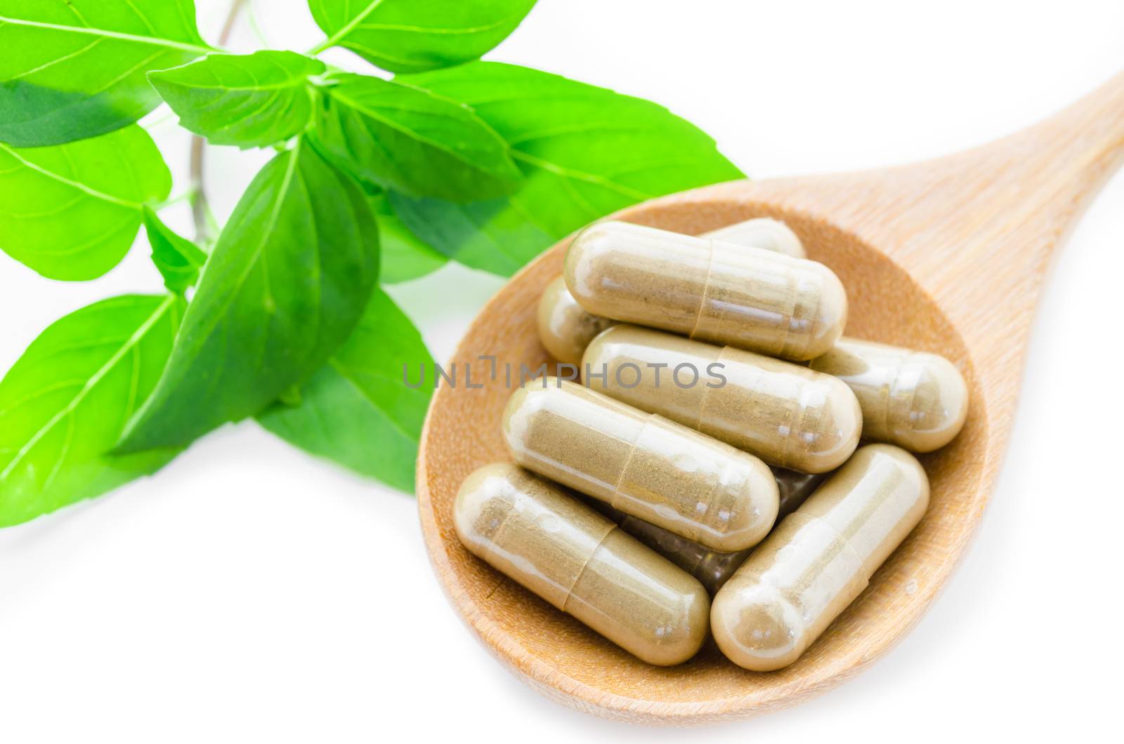 Herb capsule medicine in wooden spoon and green leaf on white background.