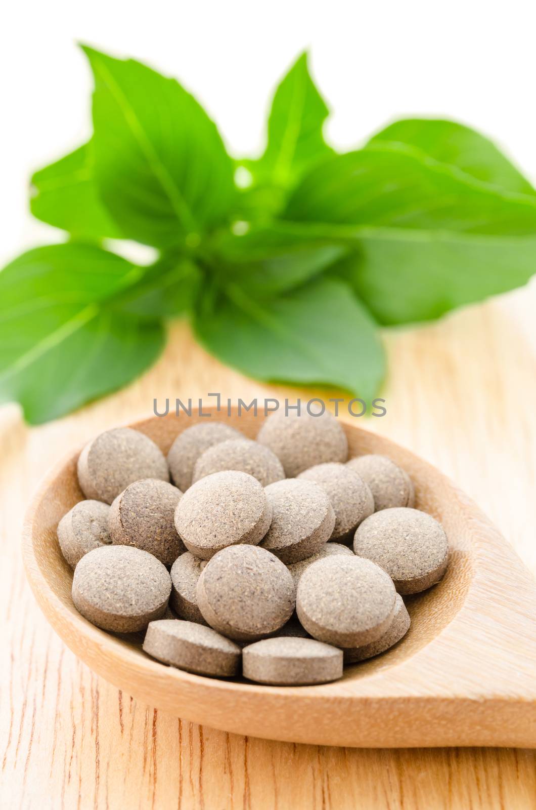 Herbal tablets in wooden spoon with green leaf on wooden background.