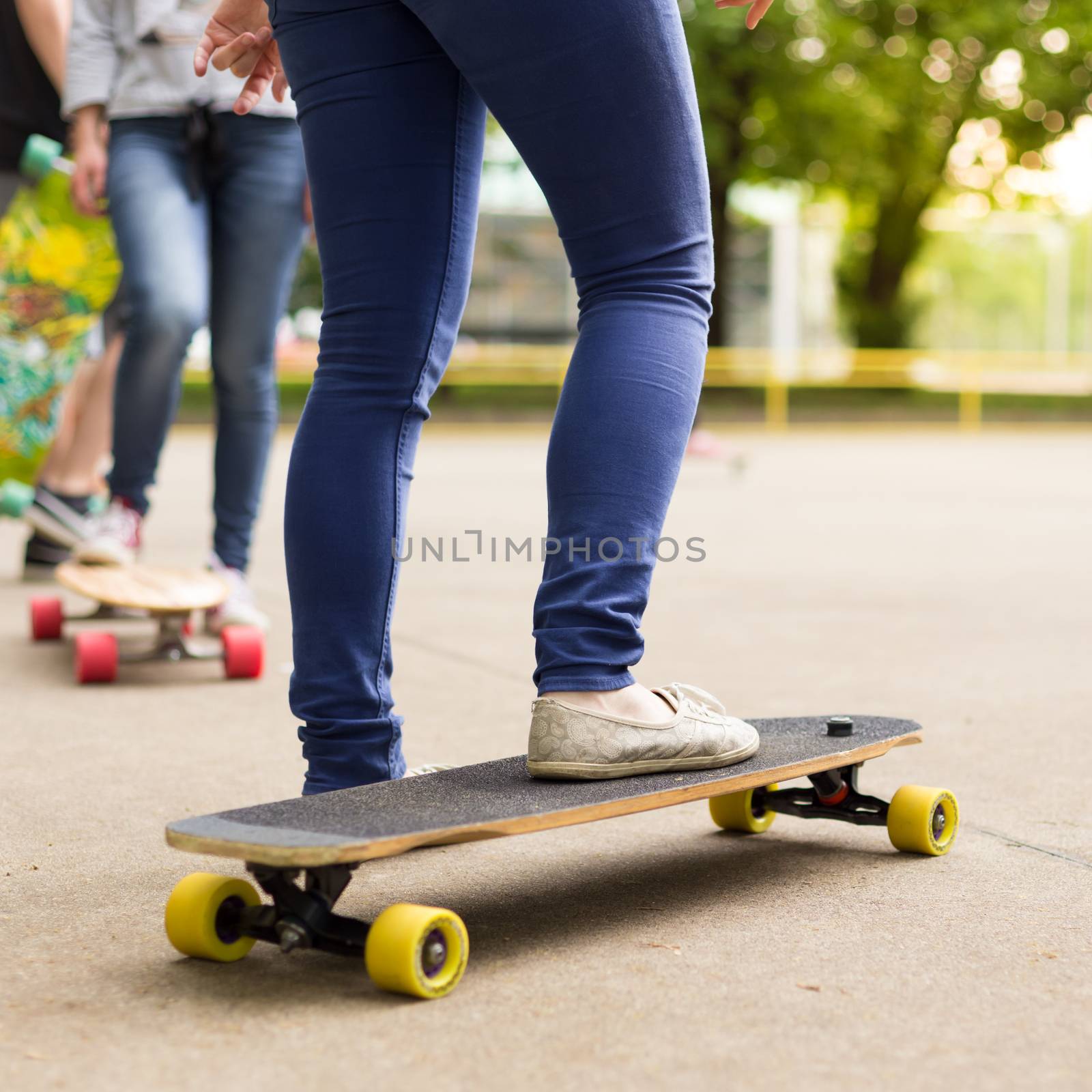 Teenage girl wearing blue jeans and sneakers practicing long board riding in skateboarding park. Active urban life. Urban subculture.
