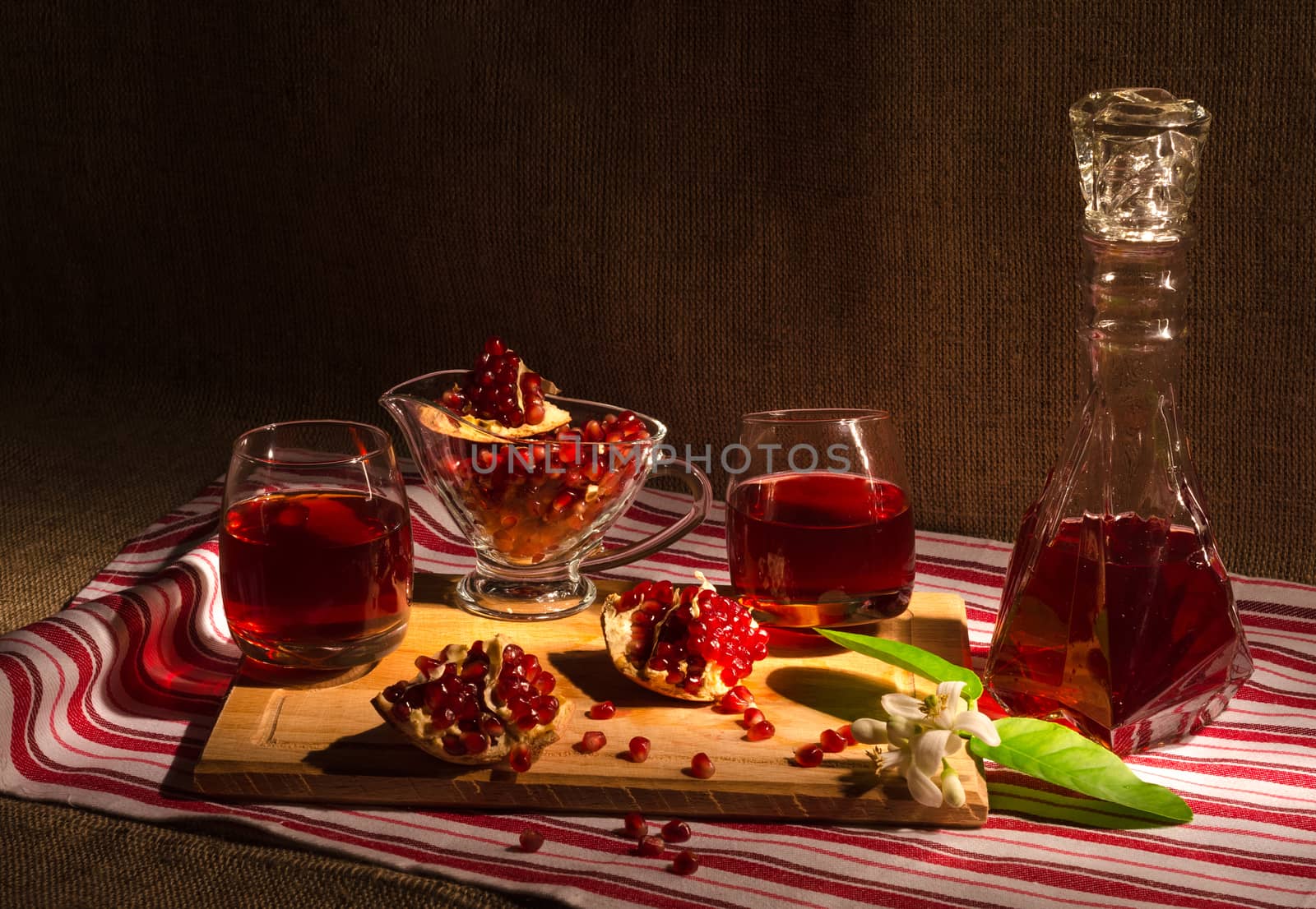 Pomegranate juice by the glass and carafe, and grains of garnet in the bowl and on a chopping Board. On the striped cloth.