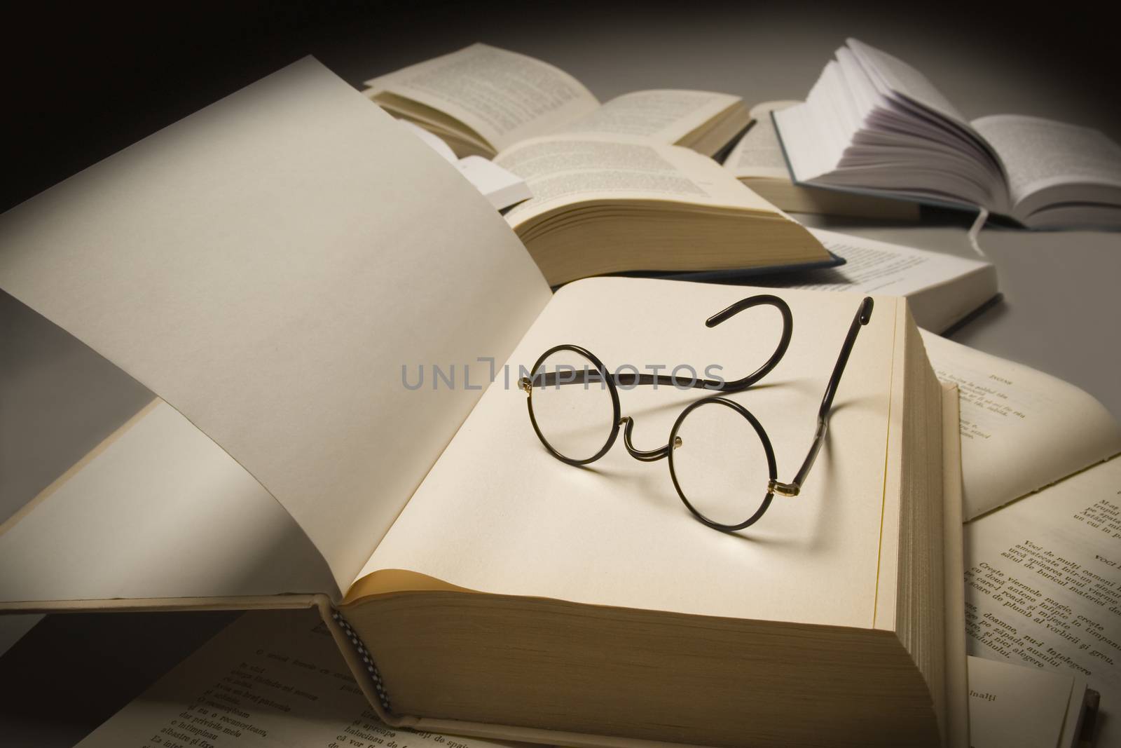 Pair of reading glasses on top of an open book, near other open books