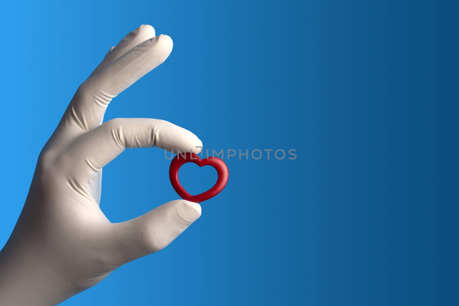 Little red heard held by a hand with a medical white glove on blue background