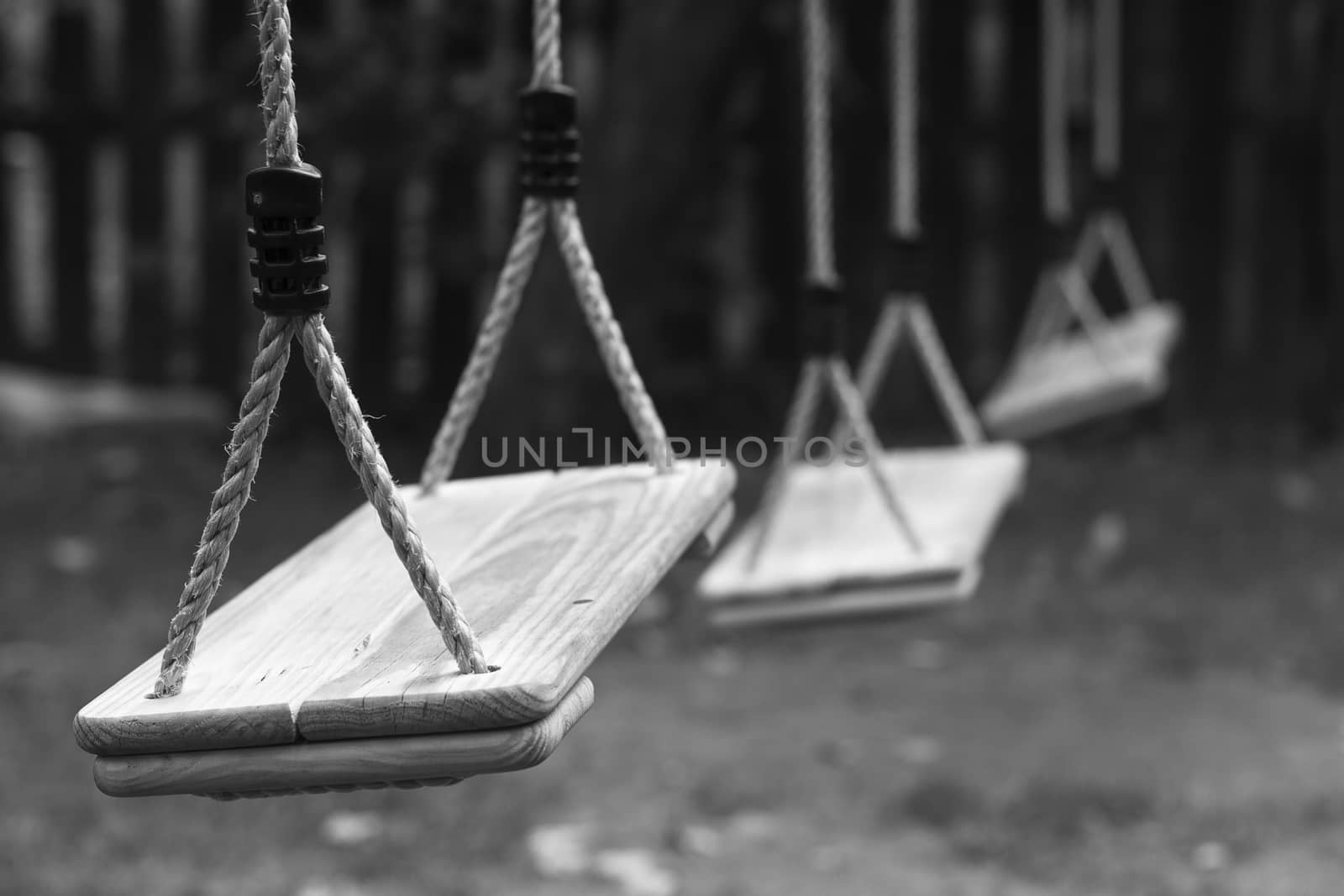 Horizontal perspective view of three wooden child swings in the park with shallow depth of field
