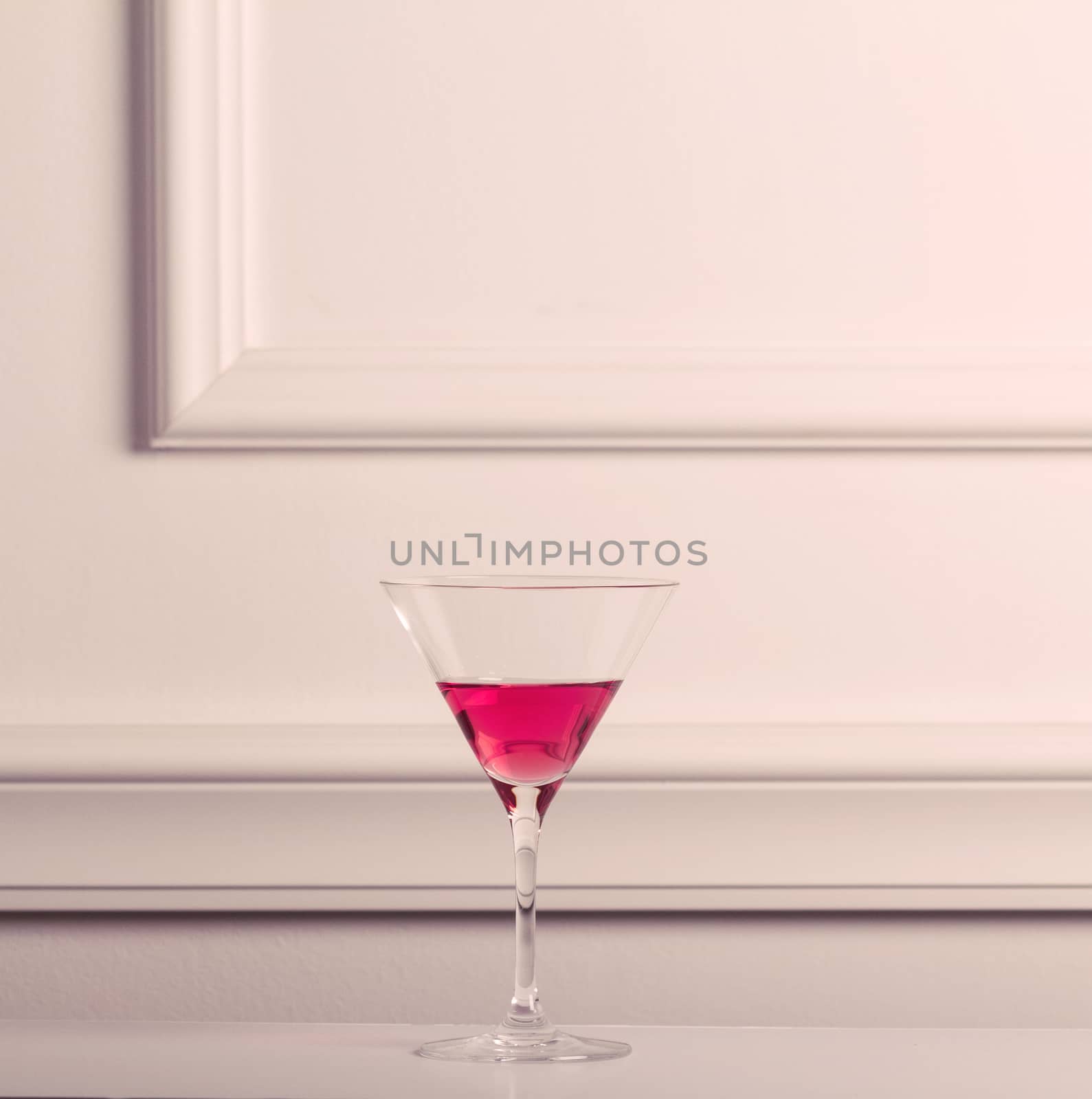 Lonely cocktail glass with pink liquid against an elegant wall.