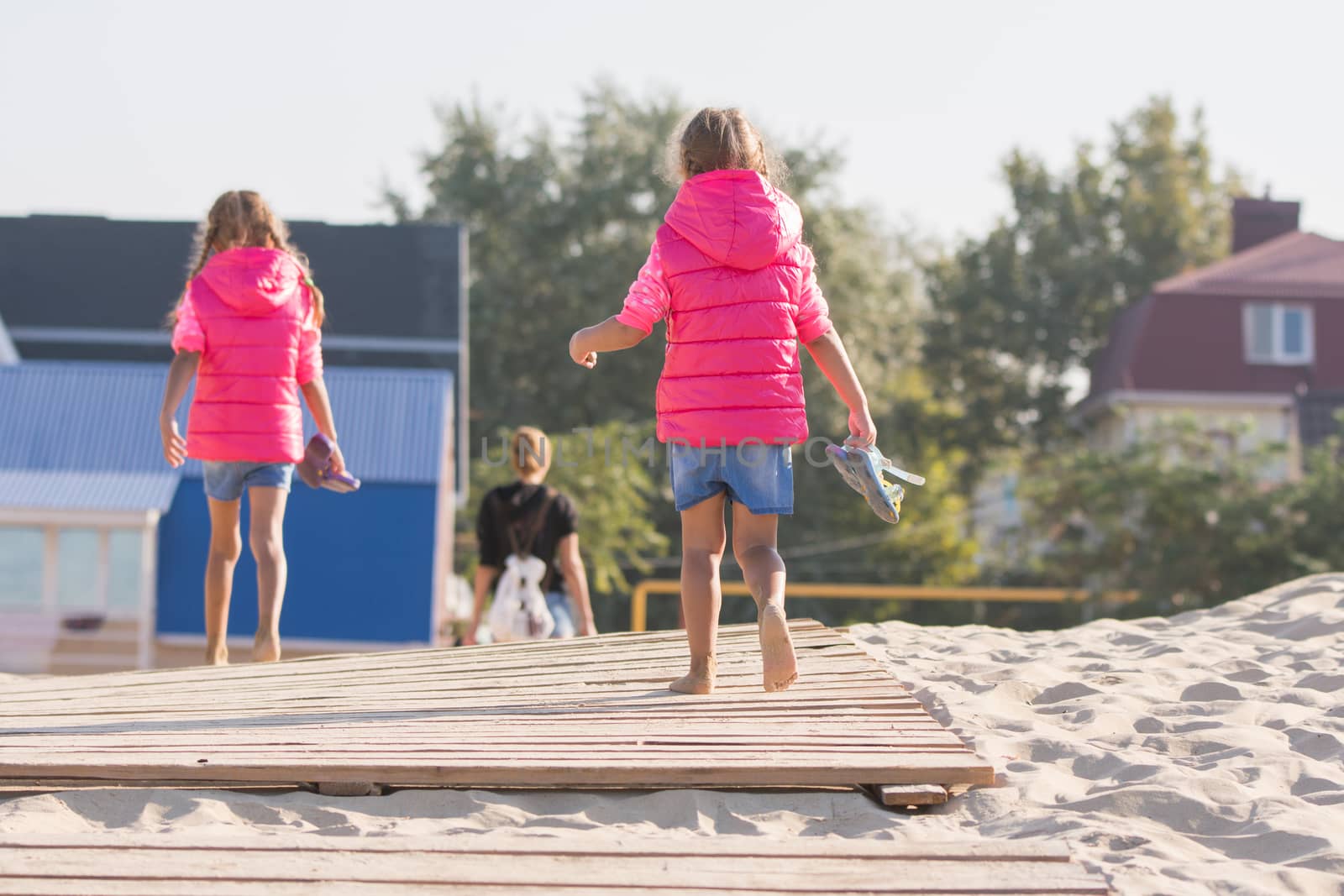 Mother and two daughters go to dawn on the wooden flooring in the sand, one girl turned