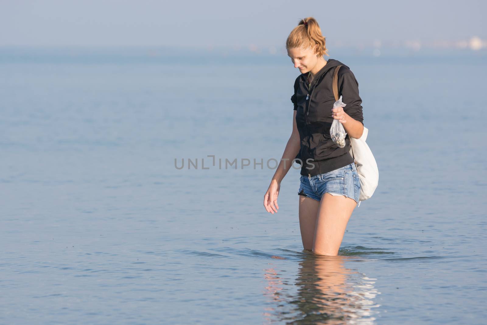 Young girl collecting seashells on the sea early in the morning and puts in a bag