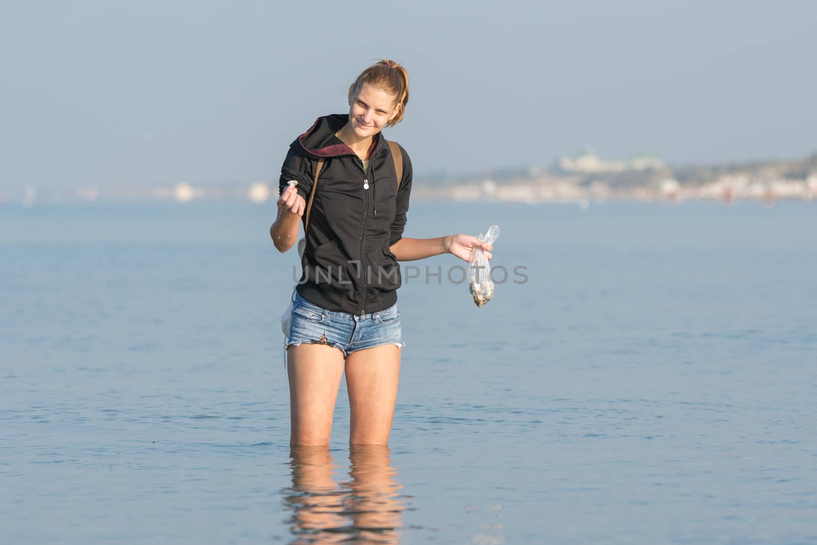 Young girl collecting seashells on the sea early in the morning and puts in a bag