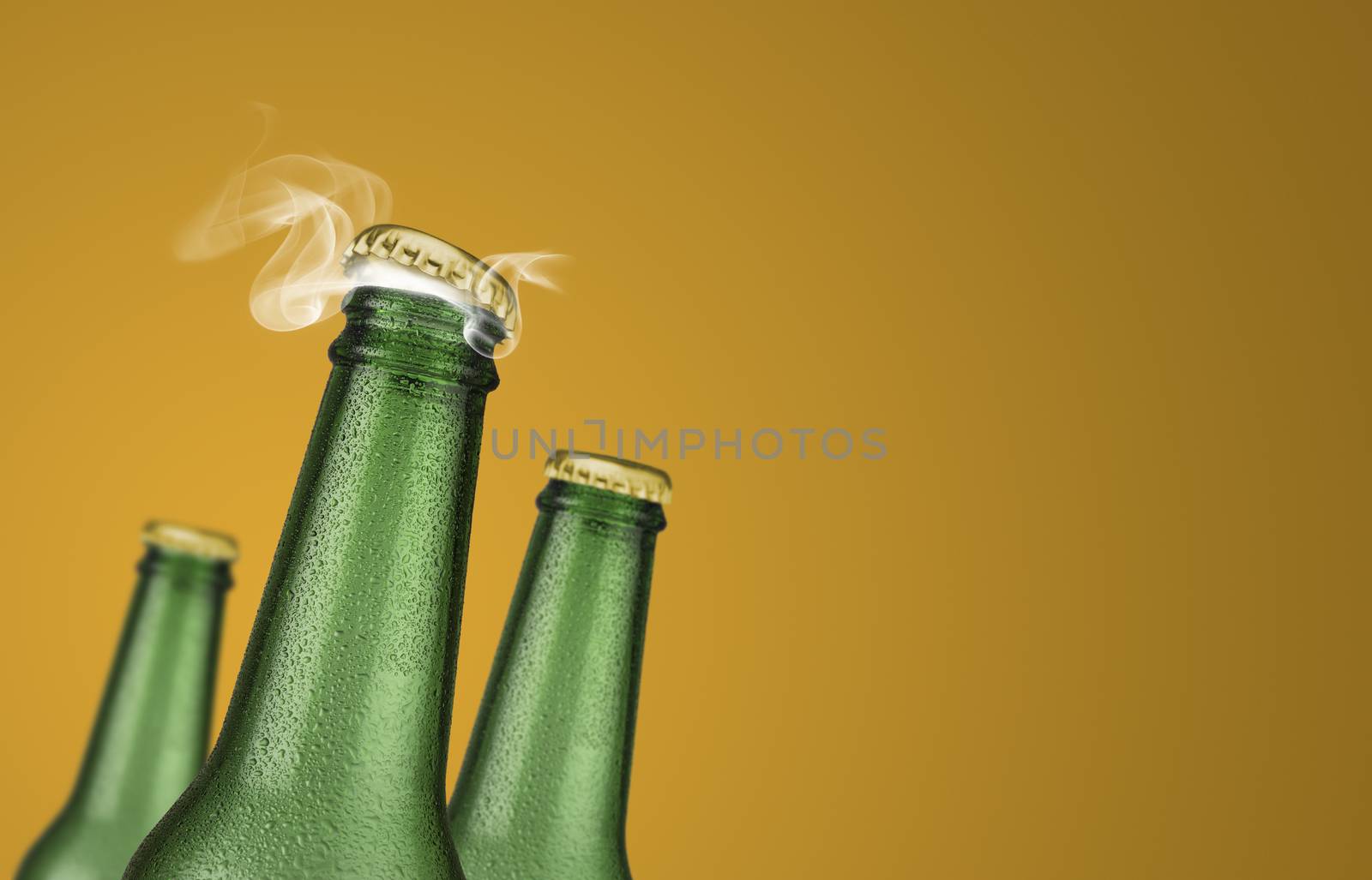Horizontal photo of three green cold beer bottles with water drops and golden cap open on yellow background