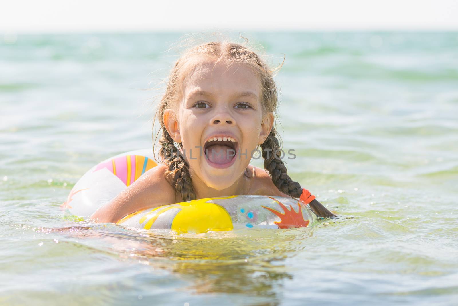 Six-year girl bathes with a swimming circle in the sea, his mouth open in pleasure