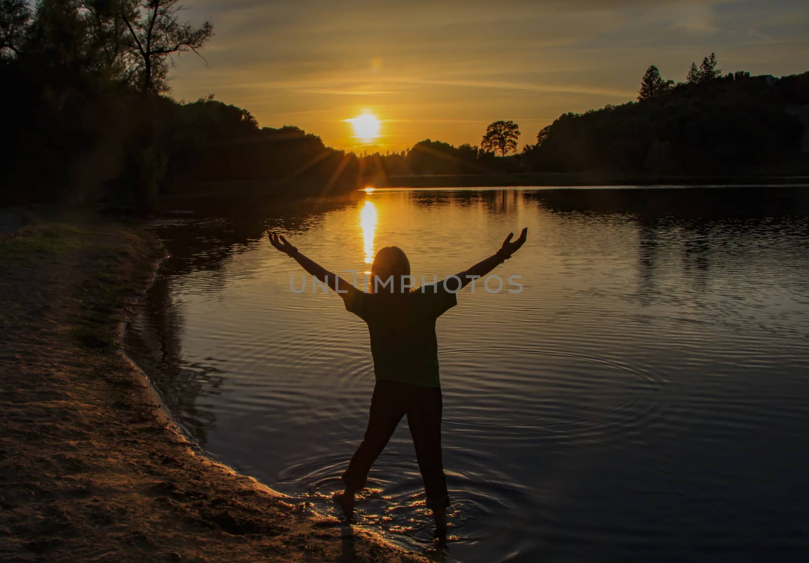 Young Girl Watching the Sun Set With Hands Raised High