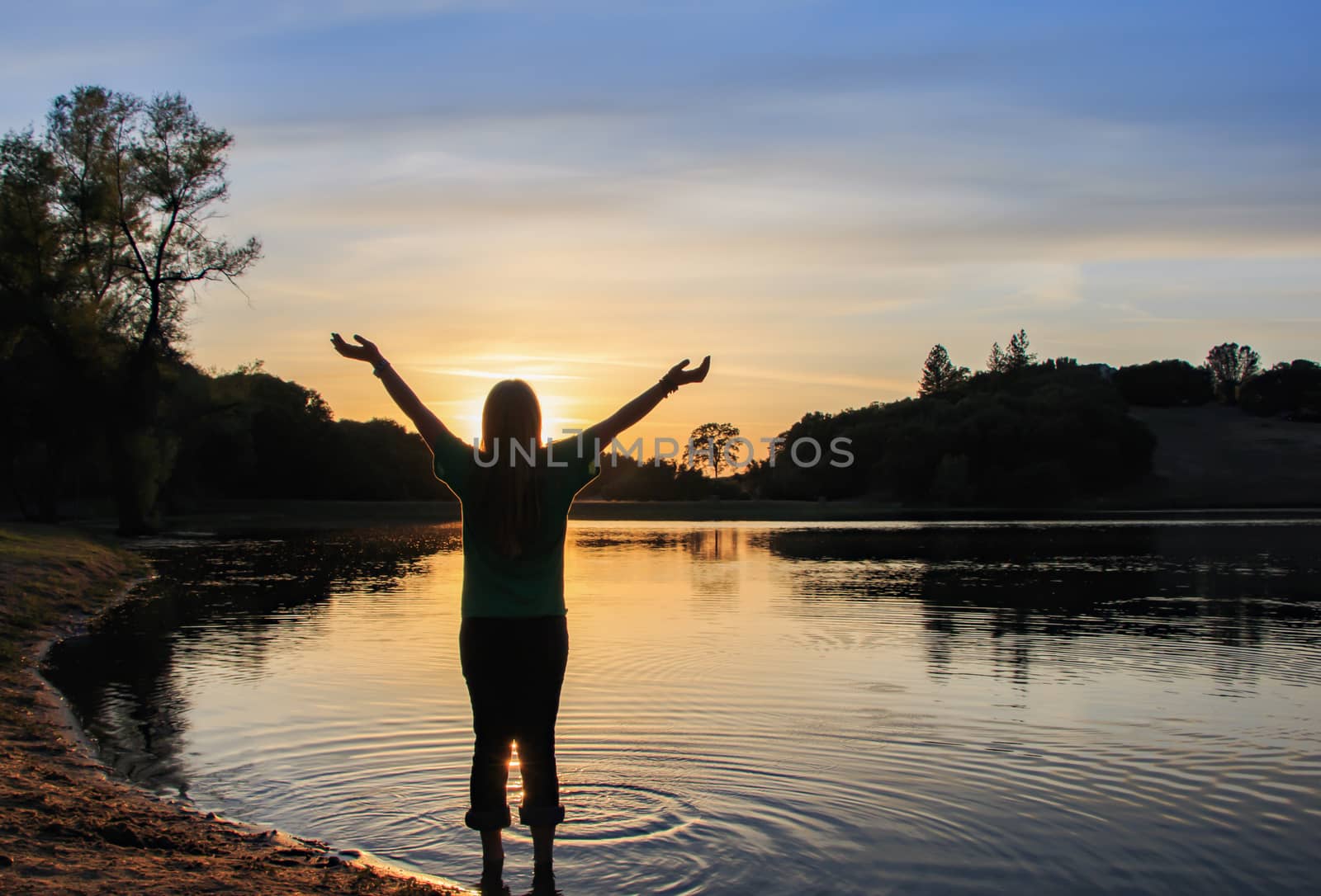 Young Girl Watching the Sun Set With Hands Raised High