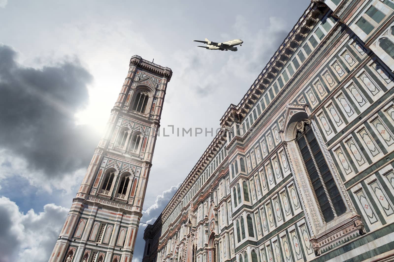 Bottom view of belfry tower of Florence Duomo, Santa Maria Del Fiore, on cloudy grey sky background with a plane.