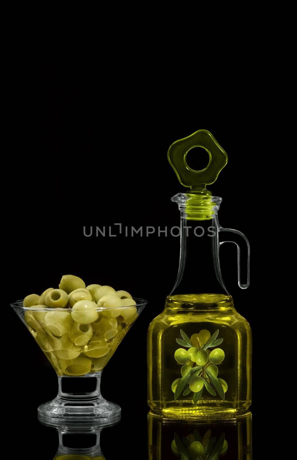 The olives in the bowl and oil in the bottle, on black background.