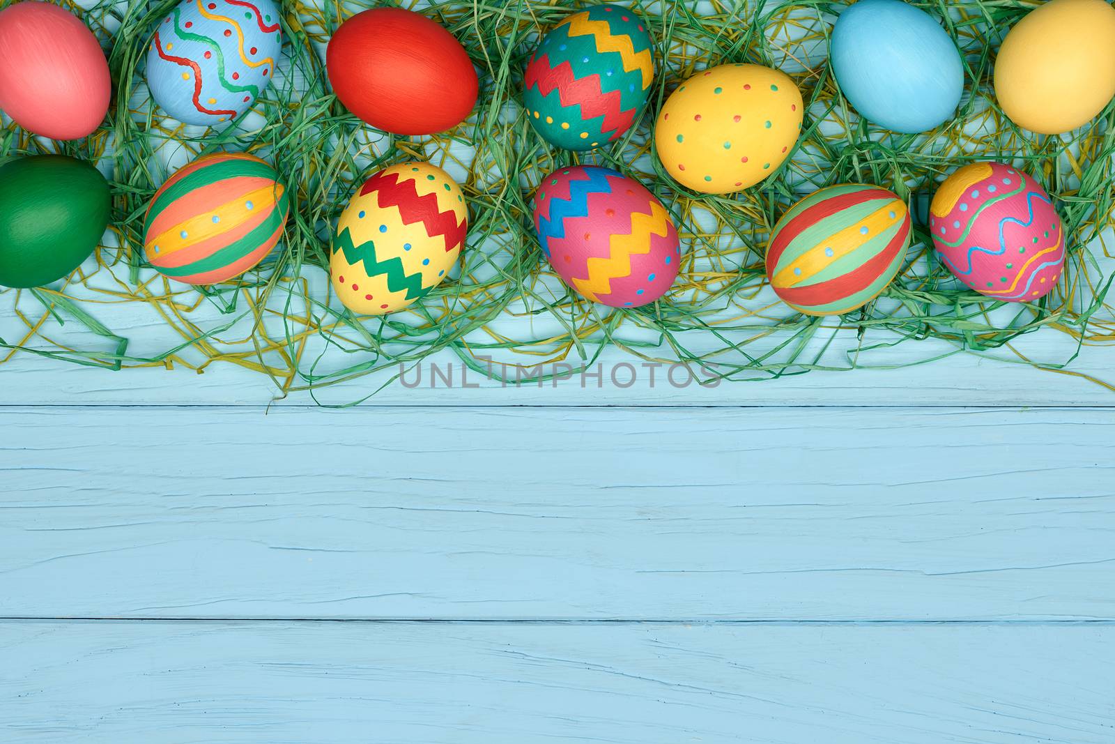 Easter eggs background. Hand painted multicolored decorated eggs on green straw, blue wood, copyspace. Unusual creative holiday greeting card 