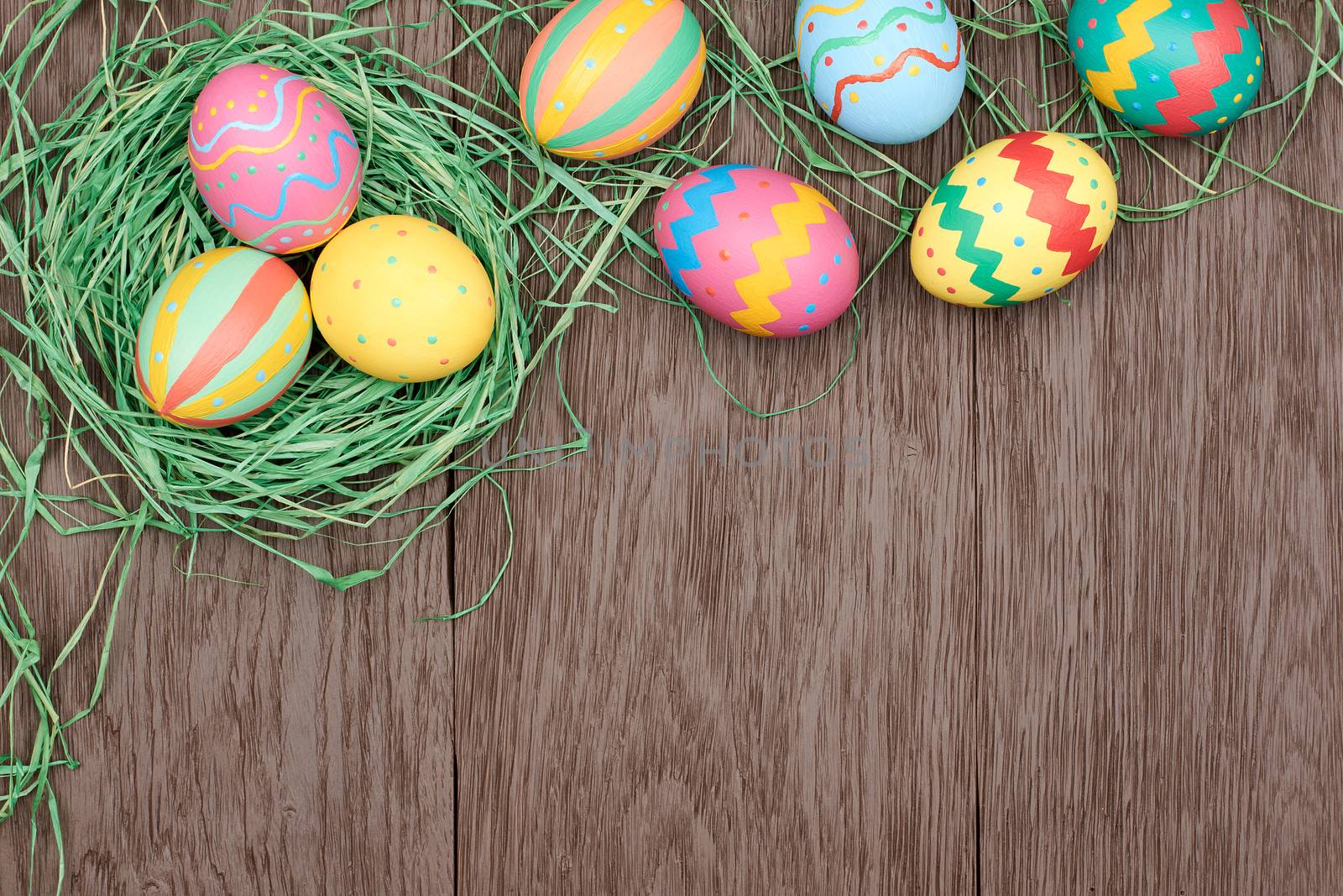 Easter eggs background. Hand painted multicolored decorated eggs on green straw nest, wood, copyspace. Unusual creative holiday greeting card 