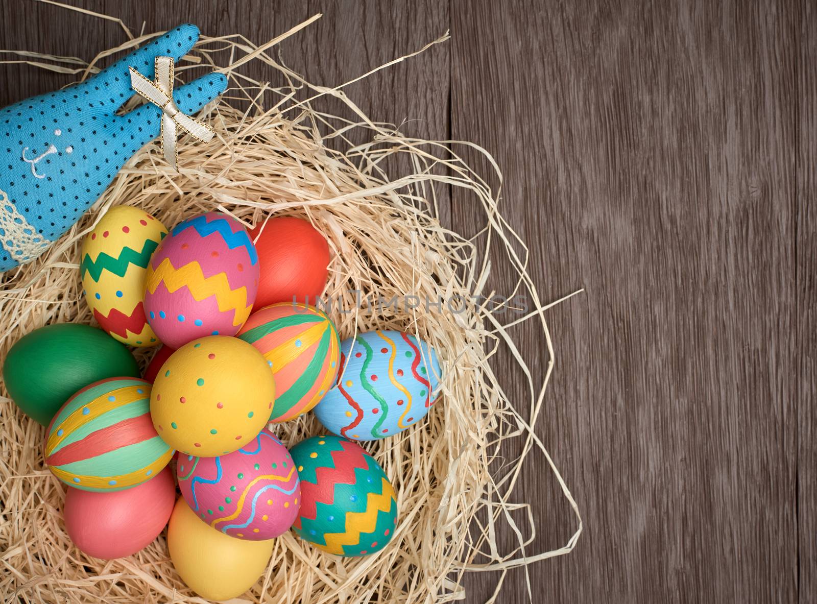 Easter eggs and rabbit. Happy bunny handmade and hand painted multicolored decorated eggs on straw nest, wooden background, copyspace. Unusual creative holiday greeting card 