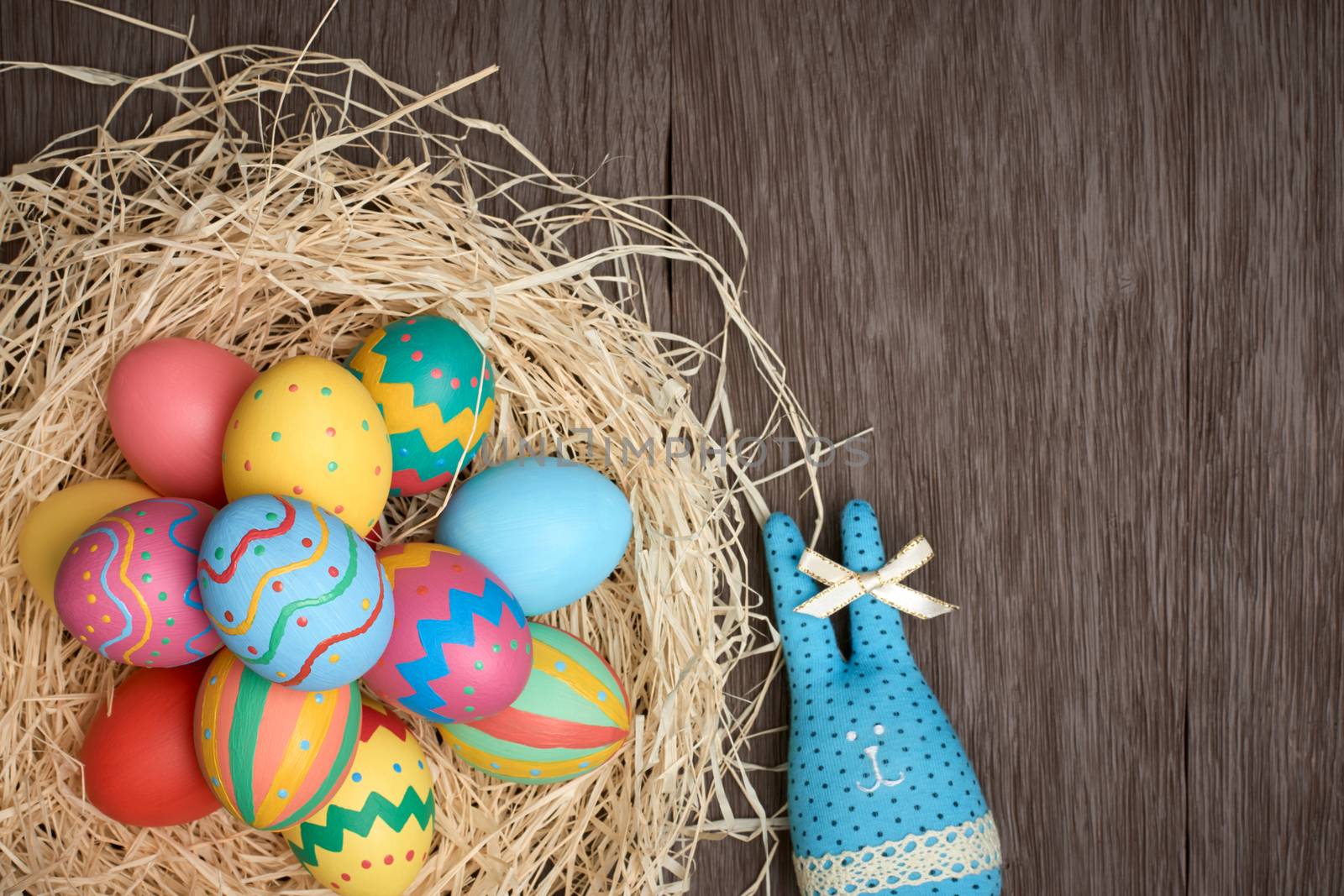 Easter eggs and rabbit. Happy bunny handmade and hand painted multicolored decorated eggs on straw nest, wooden background, copyspace. Unusual creative holiday greeting card 