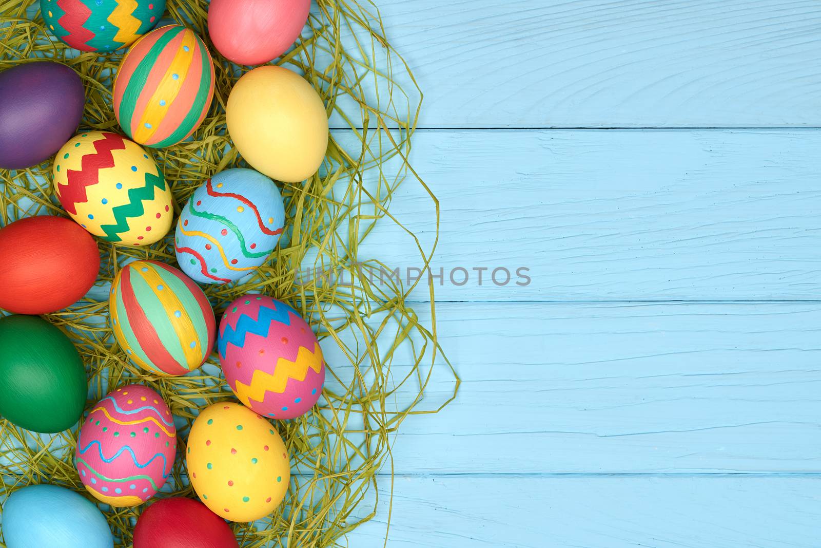 Easter eggs background. Hand painted multicolored decorated eggs on green straw, blue wood, copyspace. Unusual creative holiday greeting card 