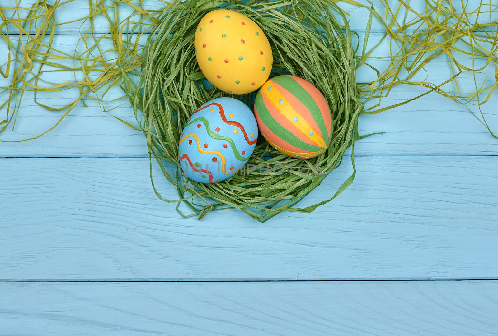 Easter eggs background. Hand painted multicolored decorated eggs on green straw nest, blue wood, copyspace. Unusual creative holiday greeting card 
