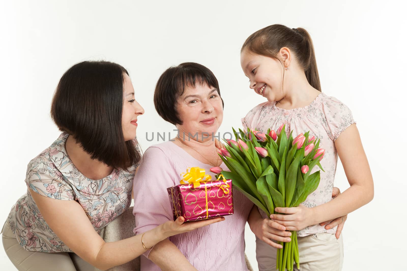 the daughter and the granddaughter give a bouquet of tulips to the grandmother