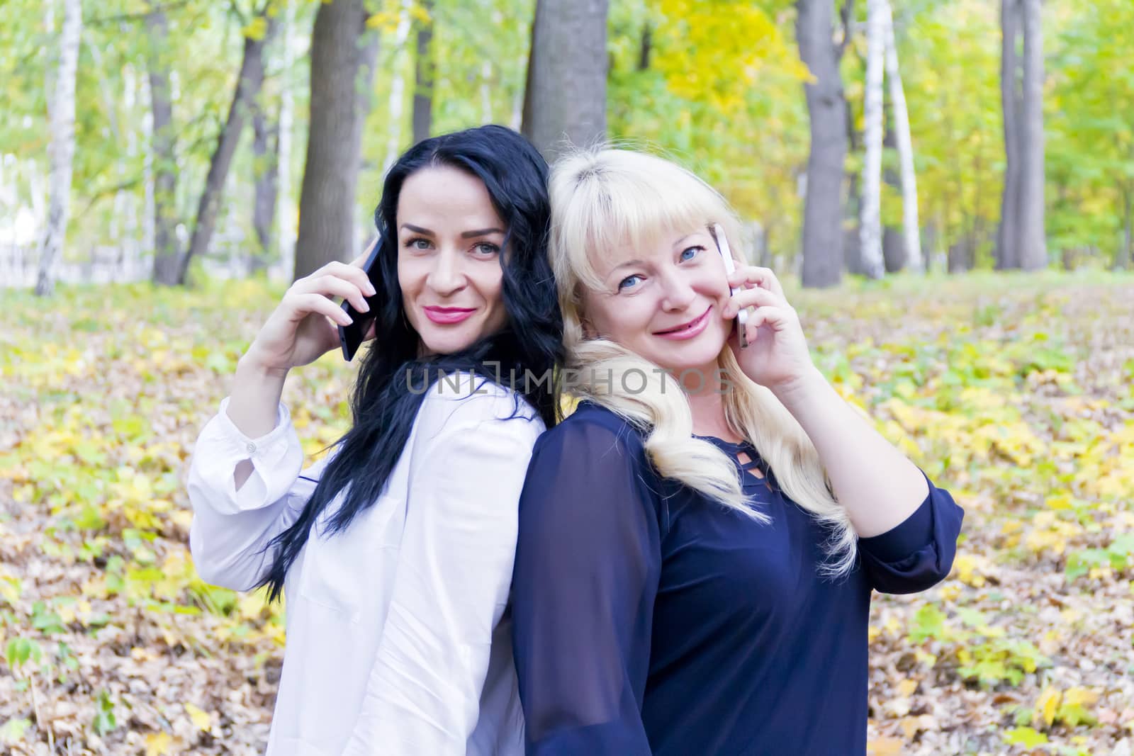 Two European women talking by mobile phone in autumn park