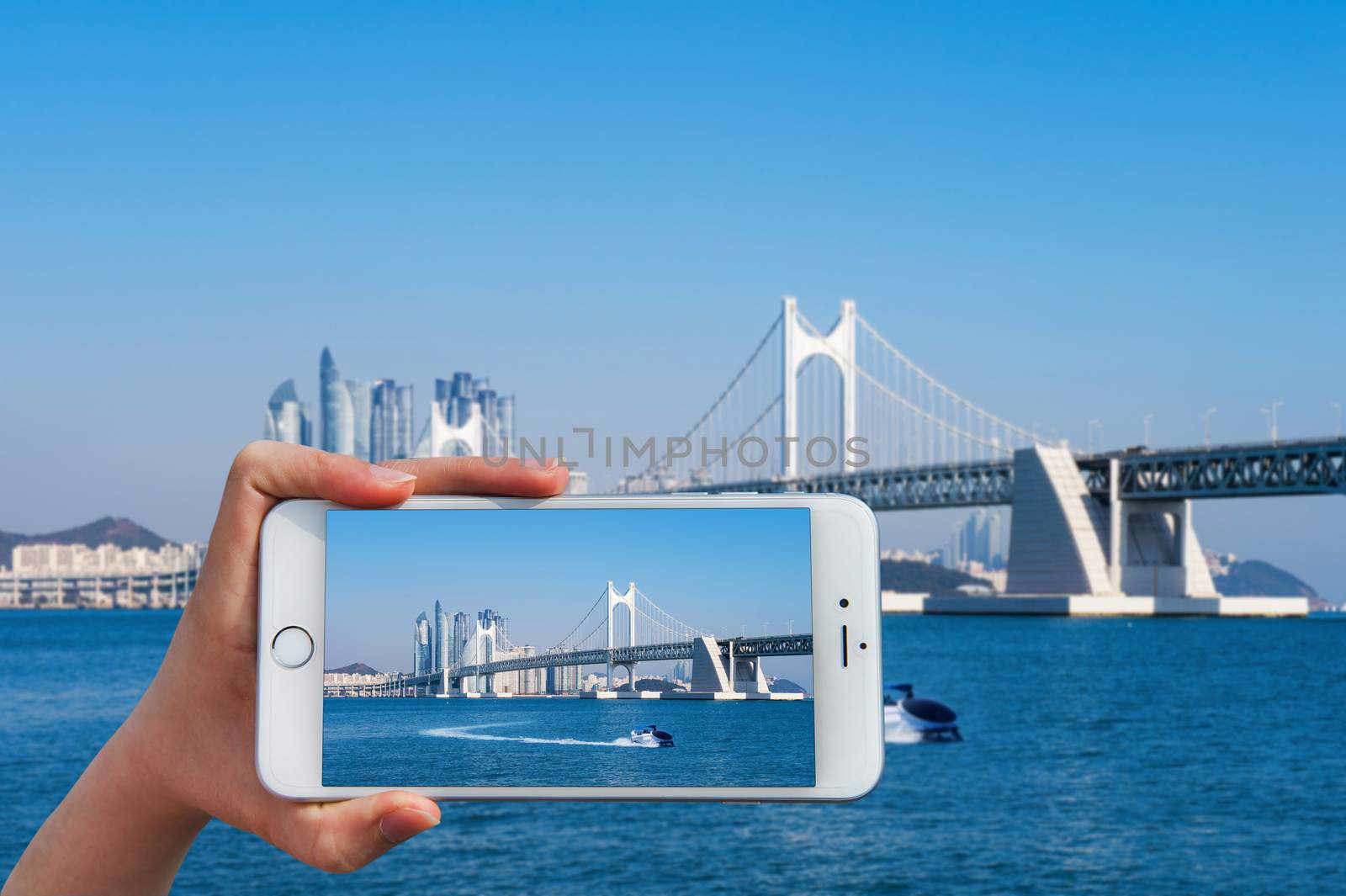 Hand holding smart phone take a photo at Gwangan bridge and Haeundae sea.