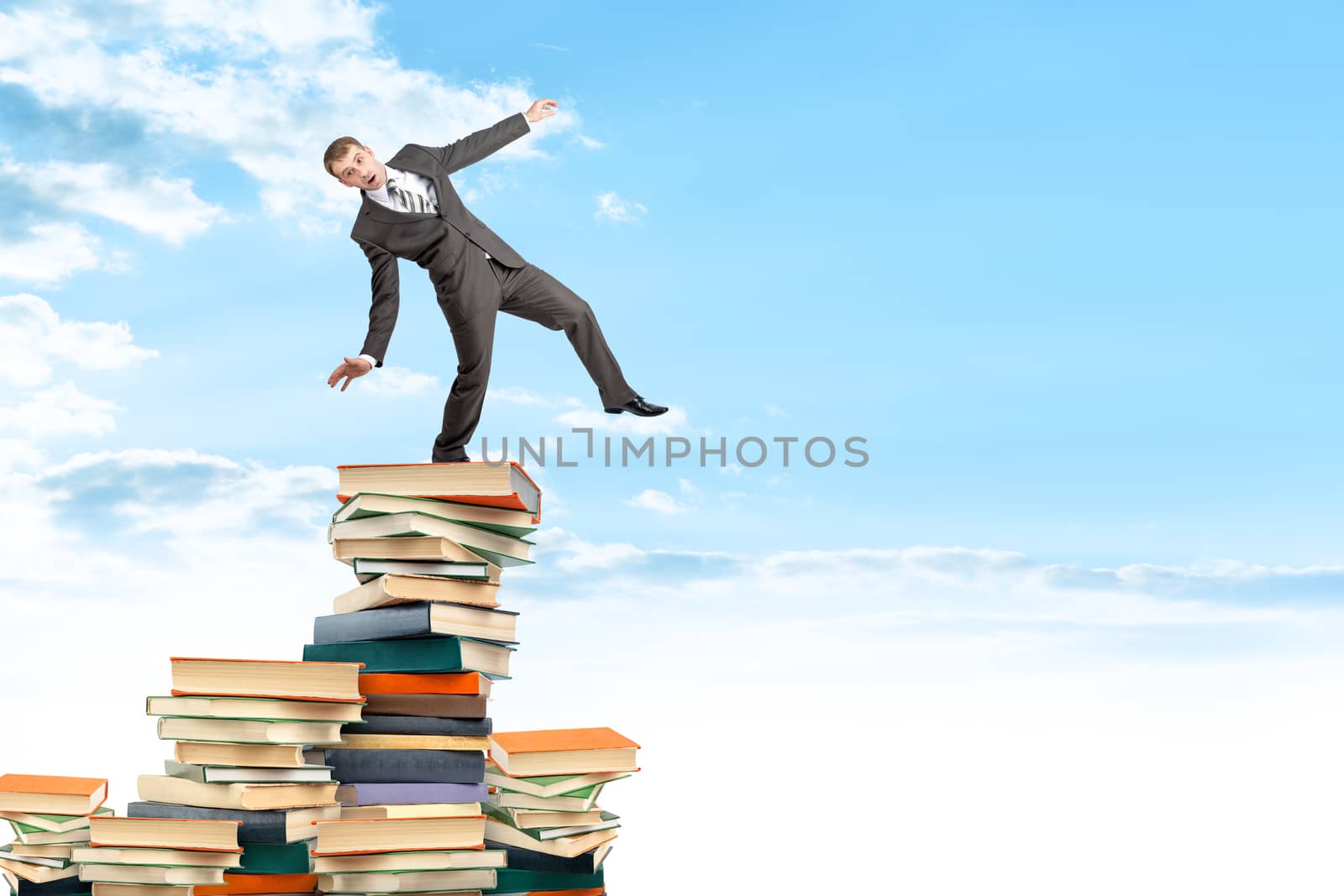 Businessman on pile of books trying not to fall, business concept