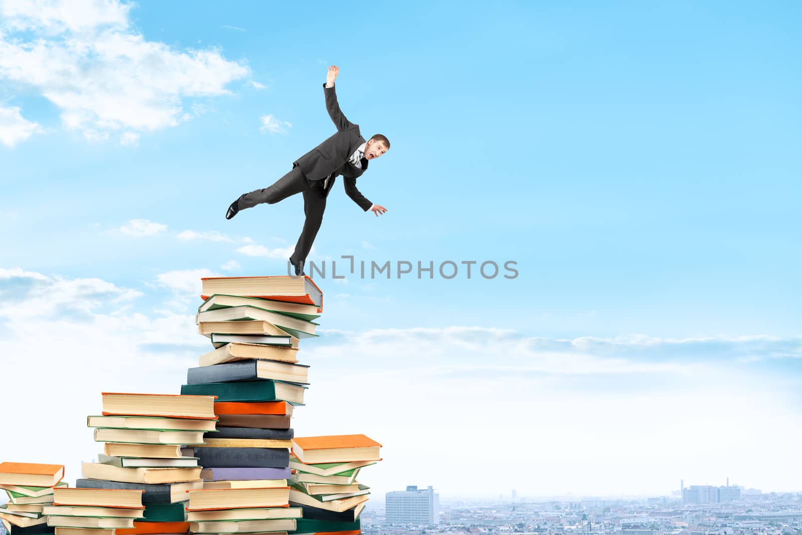 Businessman on pile of books trying not to fall, business concept