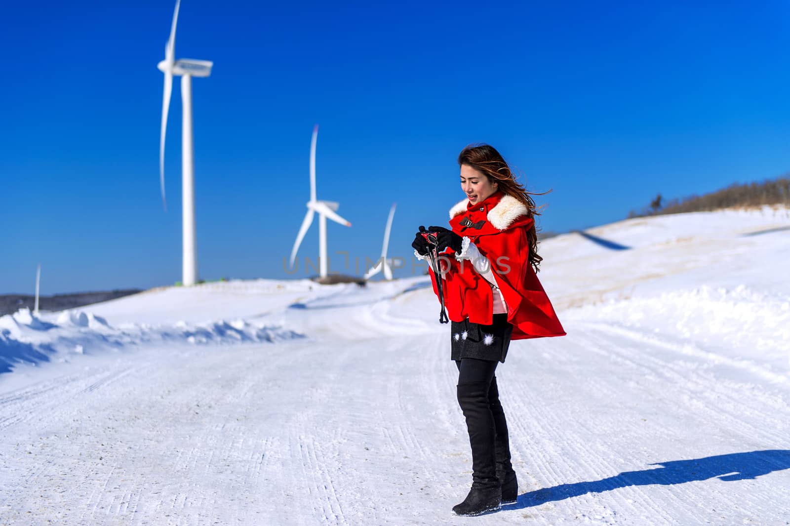 Young woman is a happiness with camera in winter of sky and winter road with snow and red dress.