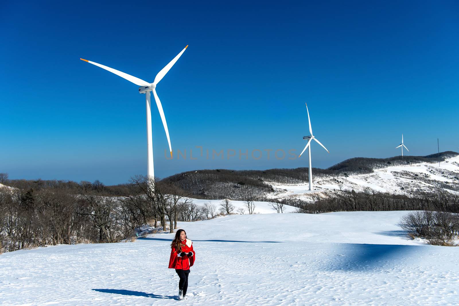 Beautiful girl walking in winter landscape of sky and winter road with snow and red dress and wind turbine.