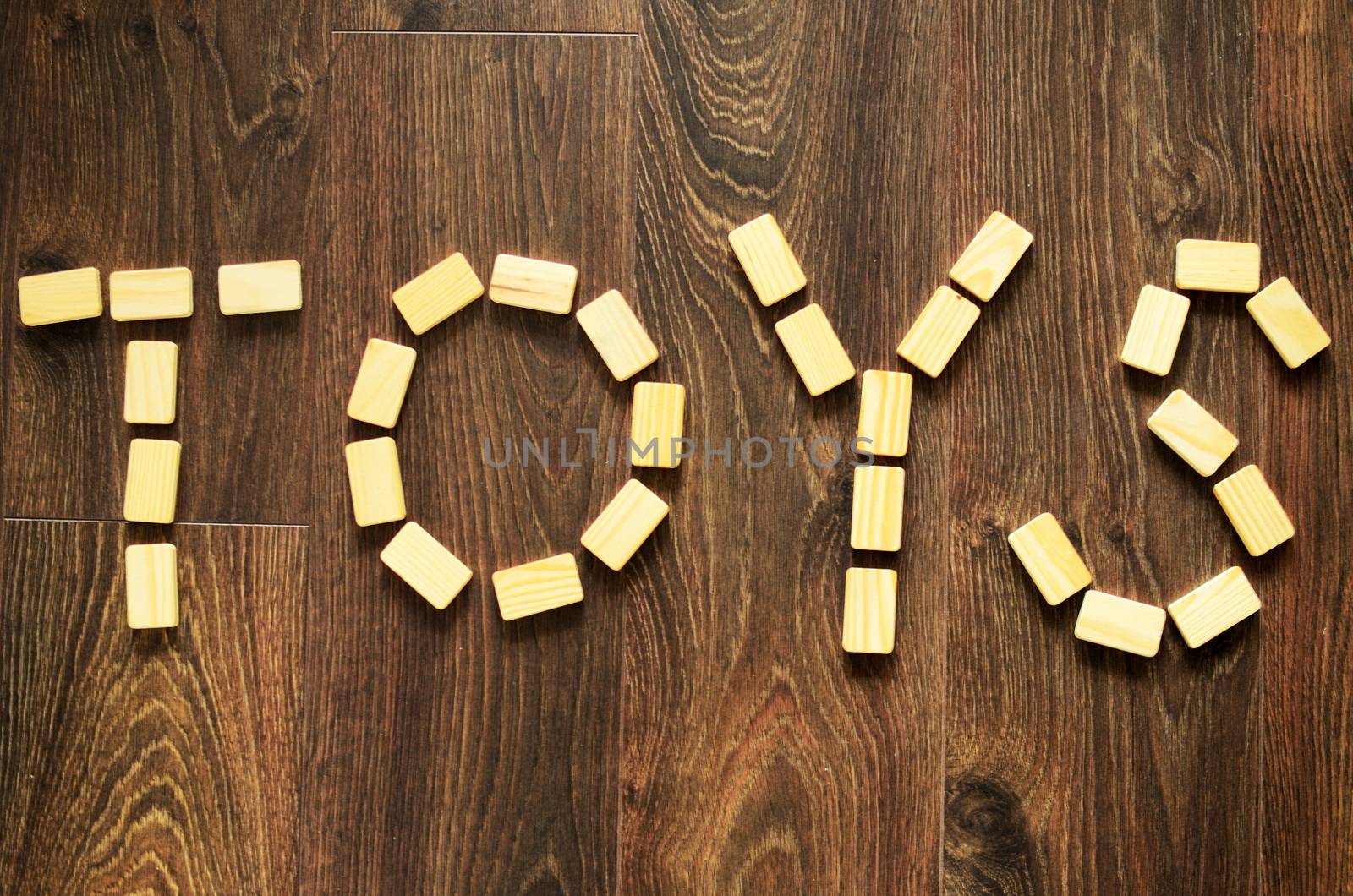 Word toys arranged by wooden blocks on wooden, brown floor.