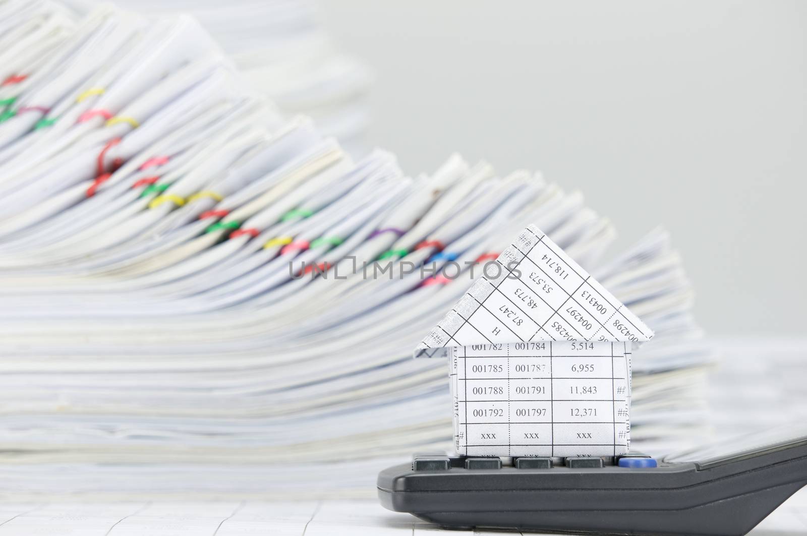 Close up house on calculator have overload of paperwork with colorful paperclip on finance account as background.