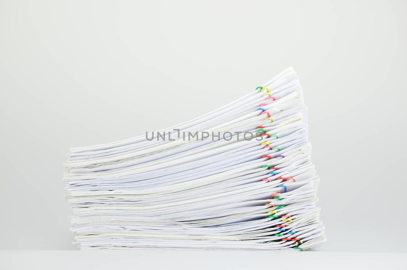 Pile of paperwork with colorful paperclip on white table as background.