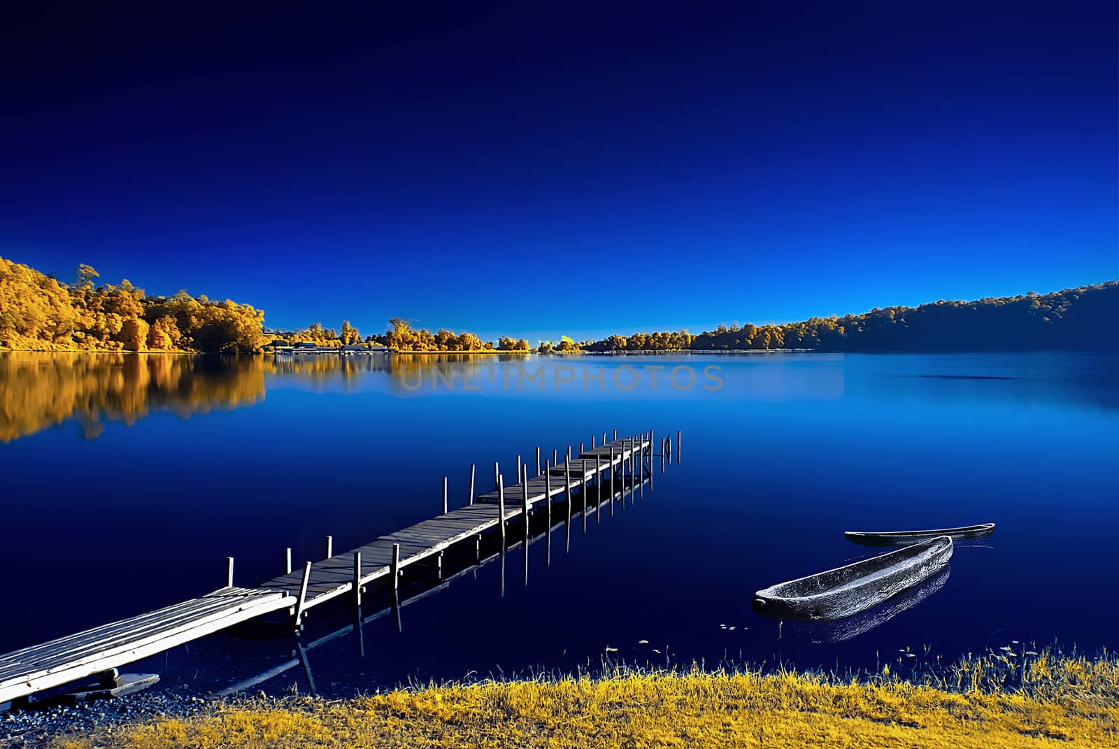 An infrared image of traditional wooden dock and a wooden boat beside and show its beautiful reflection from the water.