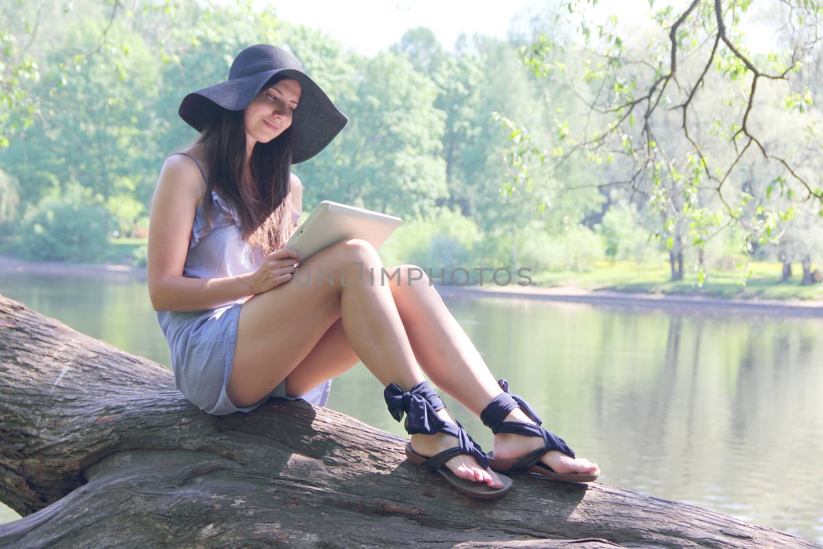 Young woman using tablet outdoor sitting on tree in park