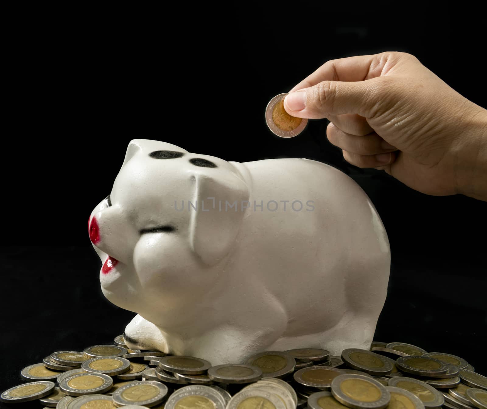 Hand to drop coin into piggy bank on black background, saving concept,investment concept,business concept.