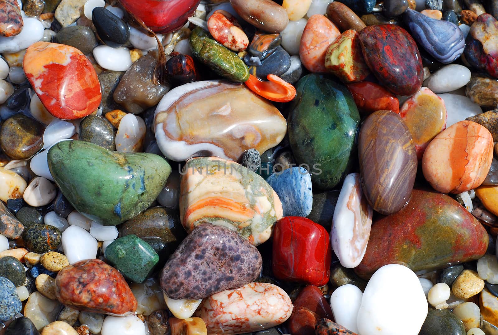 Multicolored sea pebbles in the water on the shore for background or wallpaper.